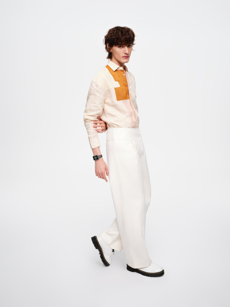 Un homme en chemise à motifs et pantalon blanc. Il marche et porte des chaussures blanches.