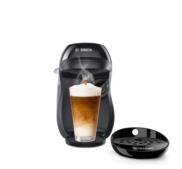 Schwarze Kaffeemaschine gibt Kaffee in ein Glas mit Milchschaum aus, mit Tablett davor.