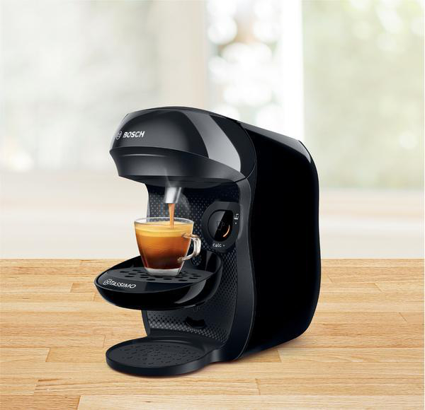 Eine schwarze Kaffeemaschine brüht Kaffee in eine transparente Glastasse auf einer Holzoberfläche.