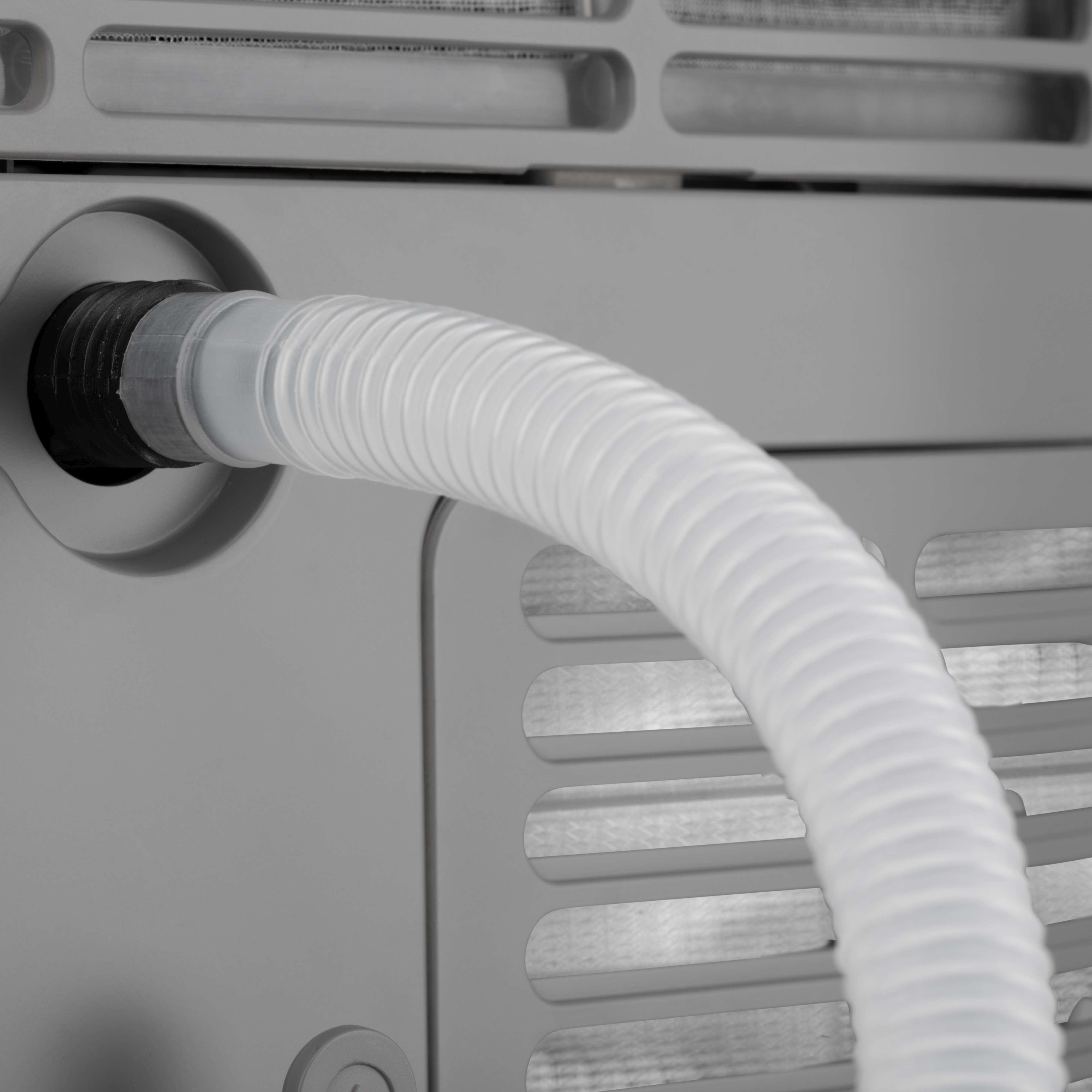 Nahaufnahme eines weißen, flexiblen Schlauchs, der mit einer grauen Klimaanlage verbunden ist.