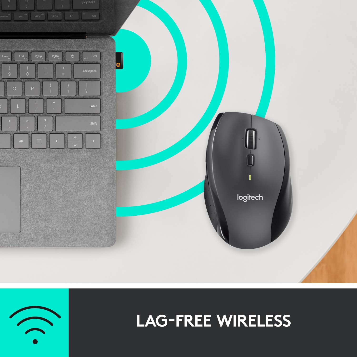 Une souris sans fil Logitech grise près d'un ordinateur portable gris sur une surface blanche.