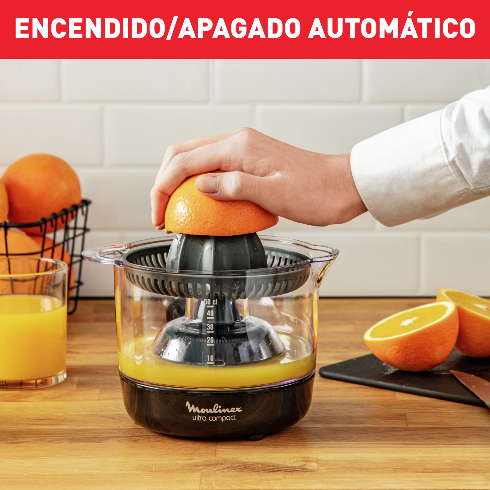 Una persona exprimiendo una naranja con una exprimidora Moulinex, con jugo de naranja y naranjas visibles.