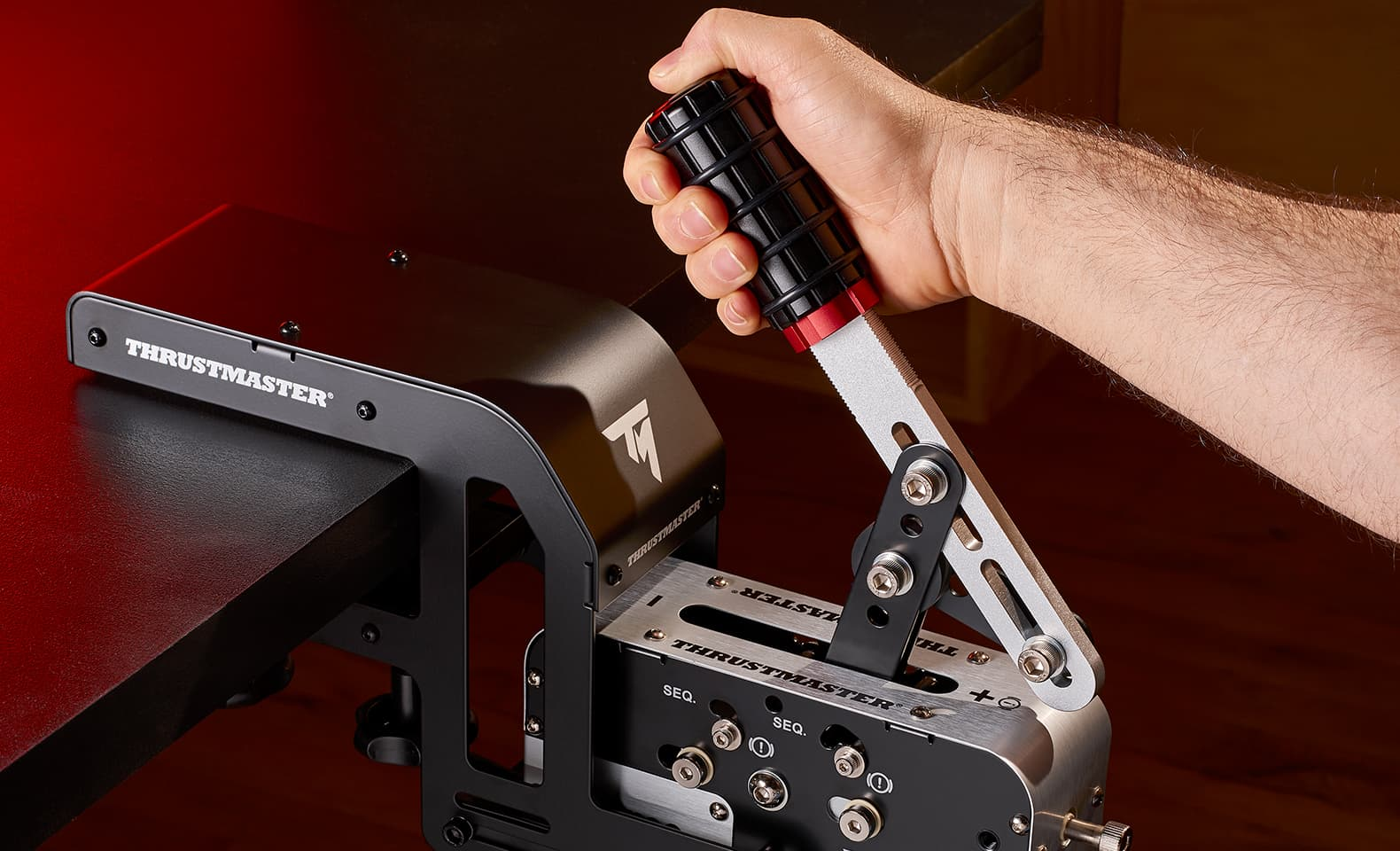 Una mano tiene la leva del cambio Thrustmaster montata su un tavolo.