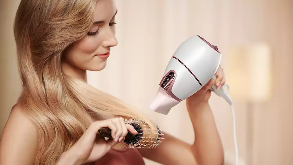 A woman is drying her hair with a hair dryer and brushing her hair with a brush.