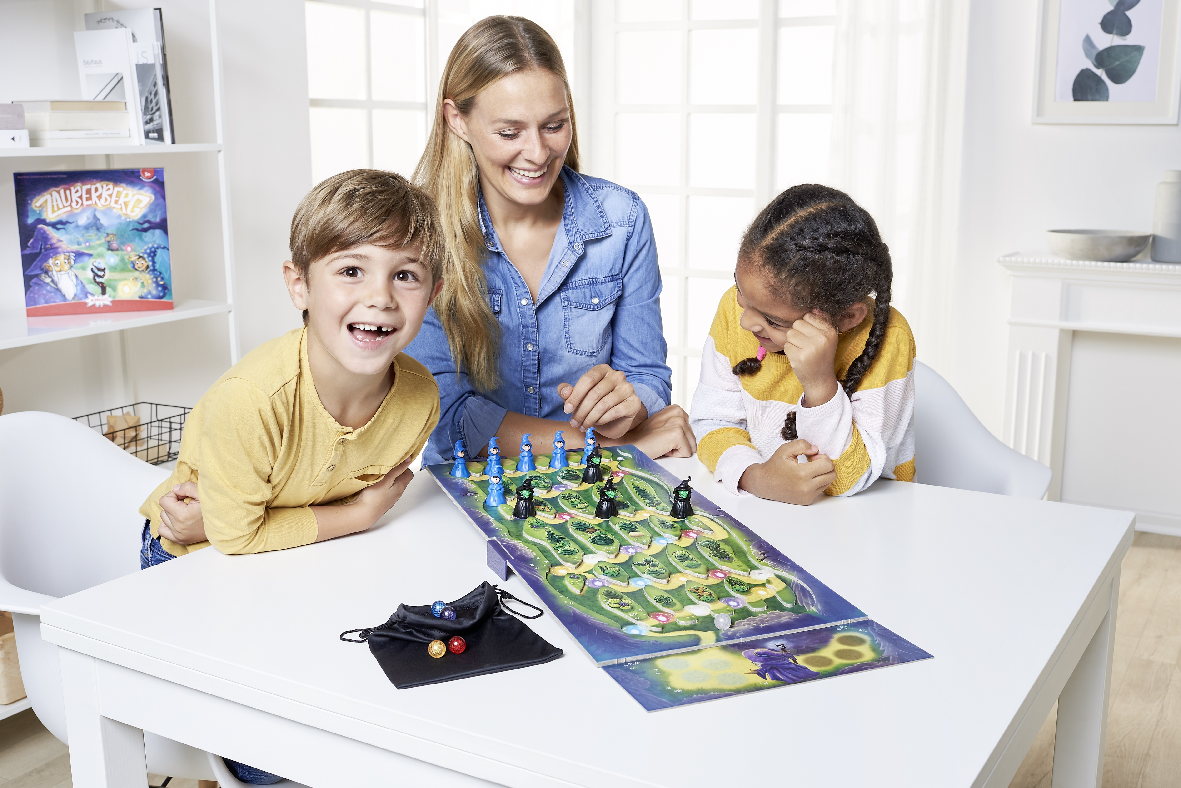 Drei Personen spielen ein Brettspiel mit Spielbrett und Spielfiguren auf einem Tisch.