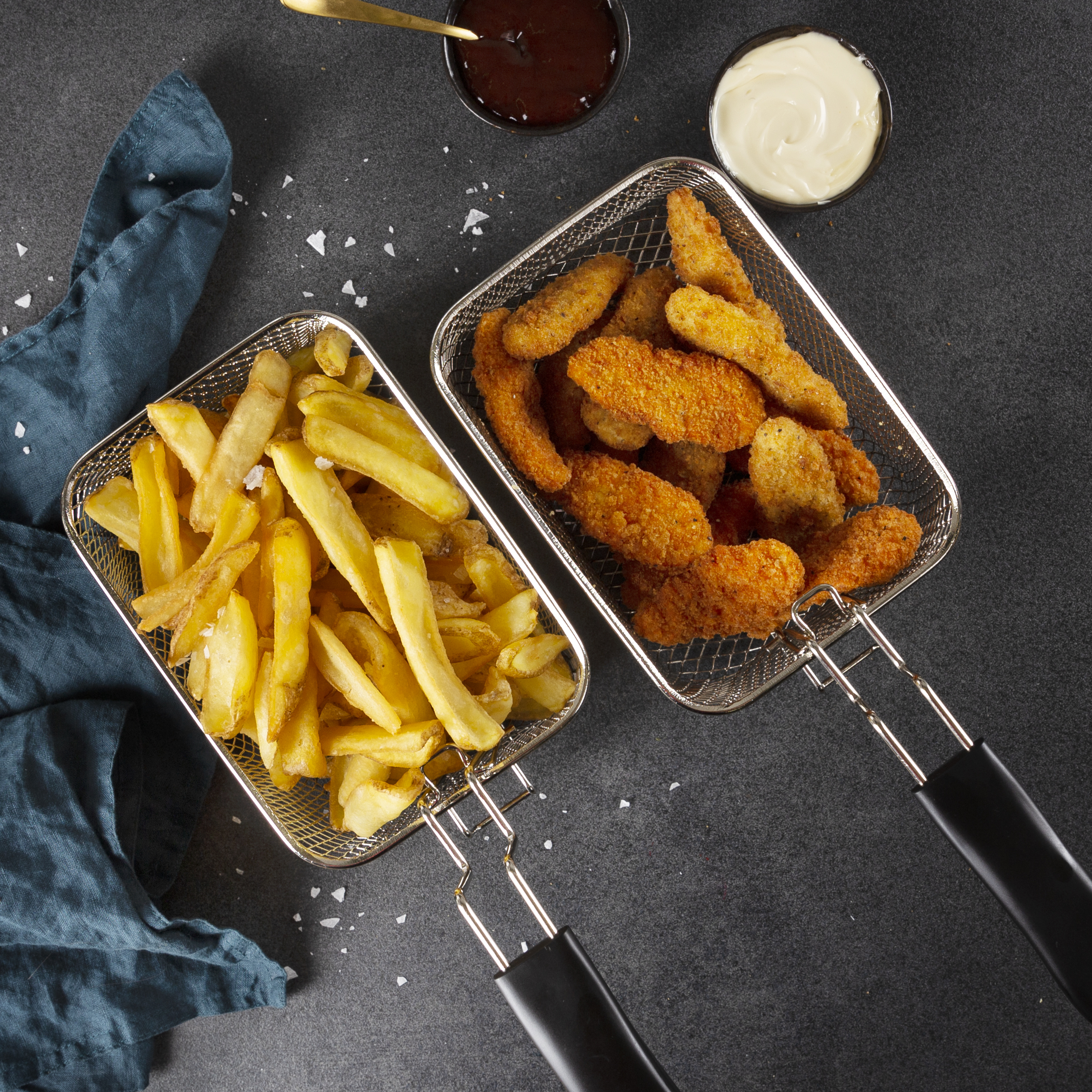 Zwei Metallkörbe mit Pommes und Chicken Nuggets, mit Saucen daneben.