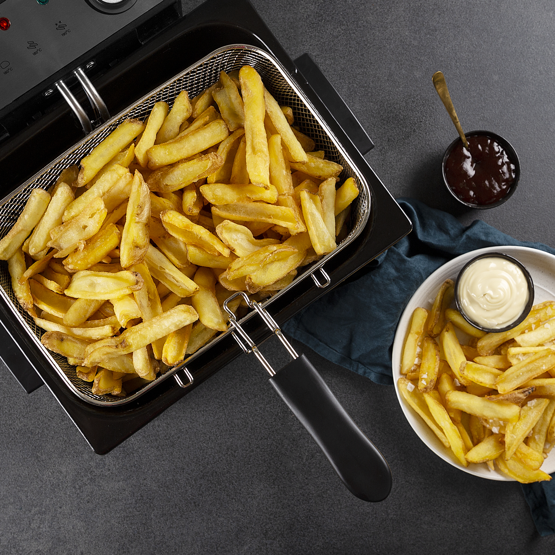Pommes in einem Korb, mit Soßen in Schalen auf einem schwarzen Tisch. Draufsicht.