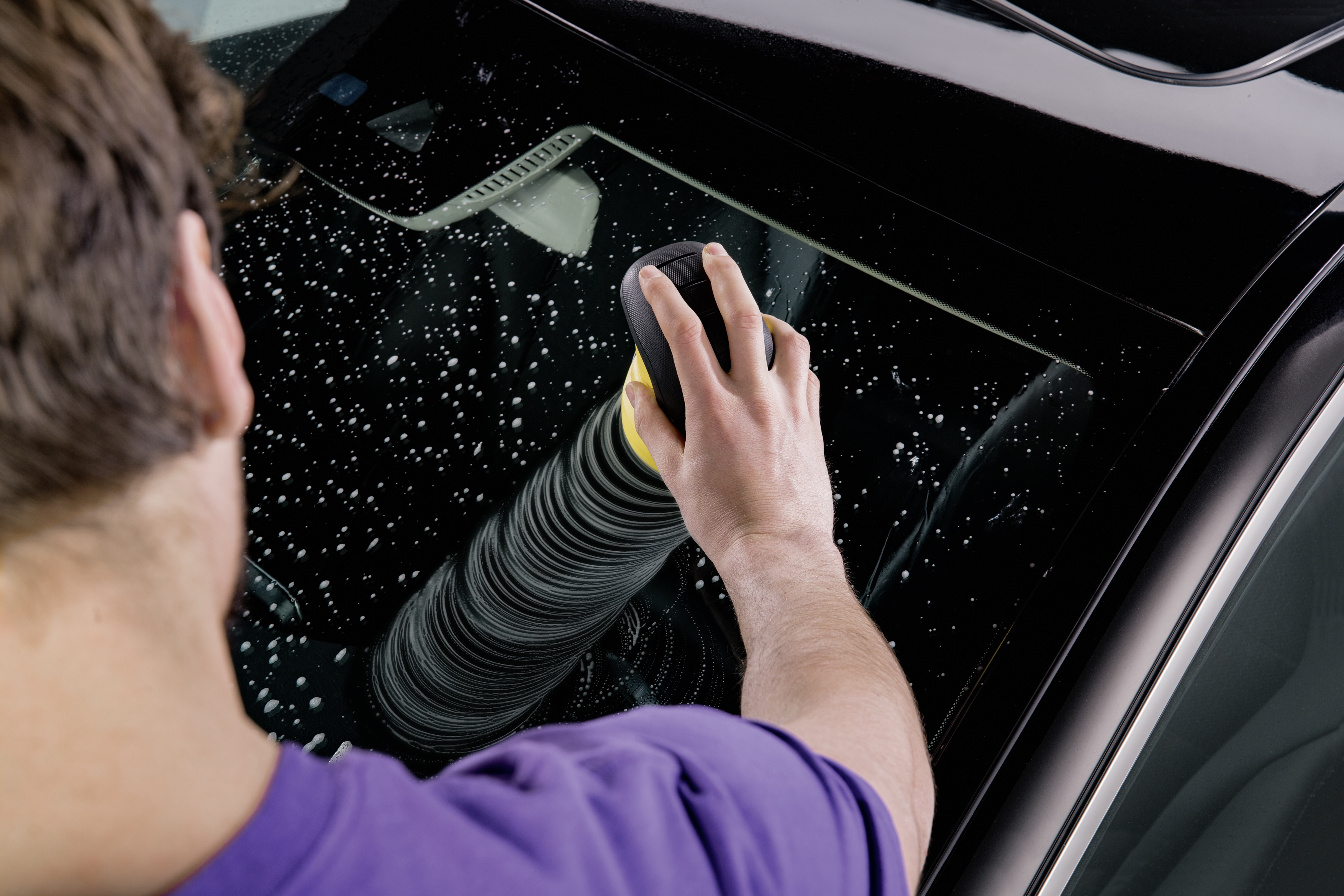 Person reinigt Autoscheibe mit einem Schrubber. Seifenwasser und Reflexion, Nahaufnahme.