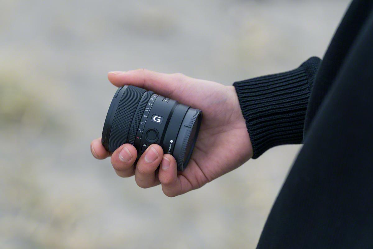 Eine Person, die ein schwarzes Kameraobjektiv in der Hand hält.