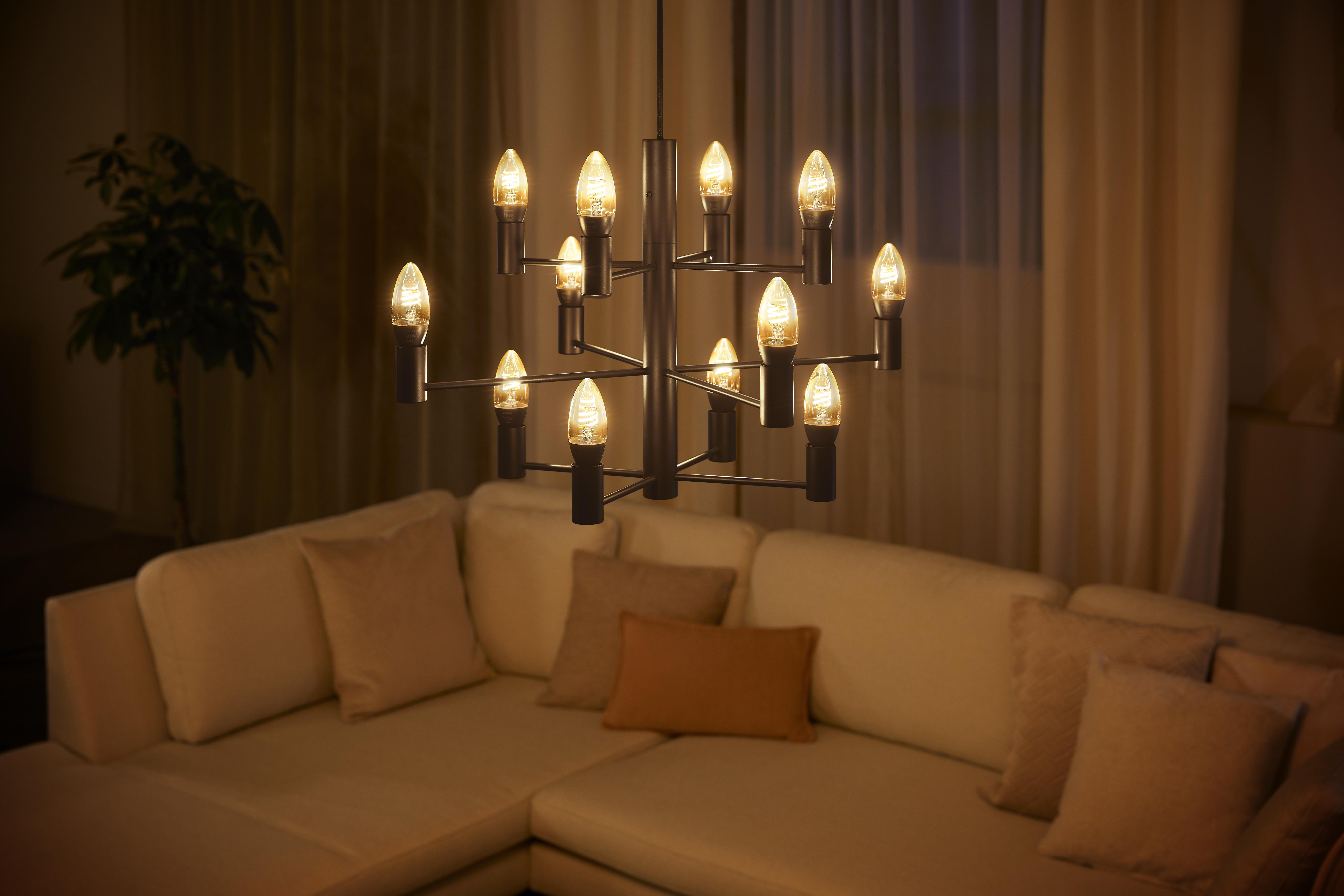Kronleuchter mit mehreren kerzenförmigen Lichtern, über einem beigen Sofa hängend.