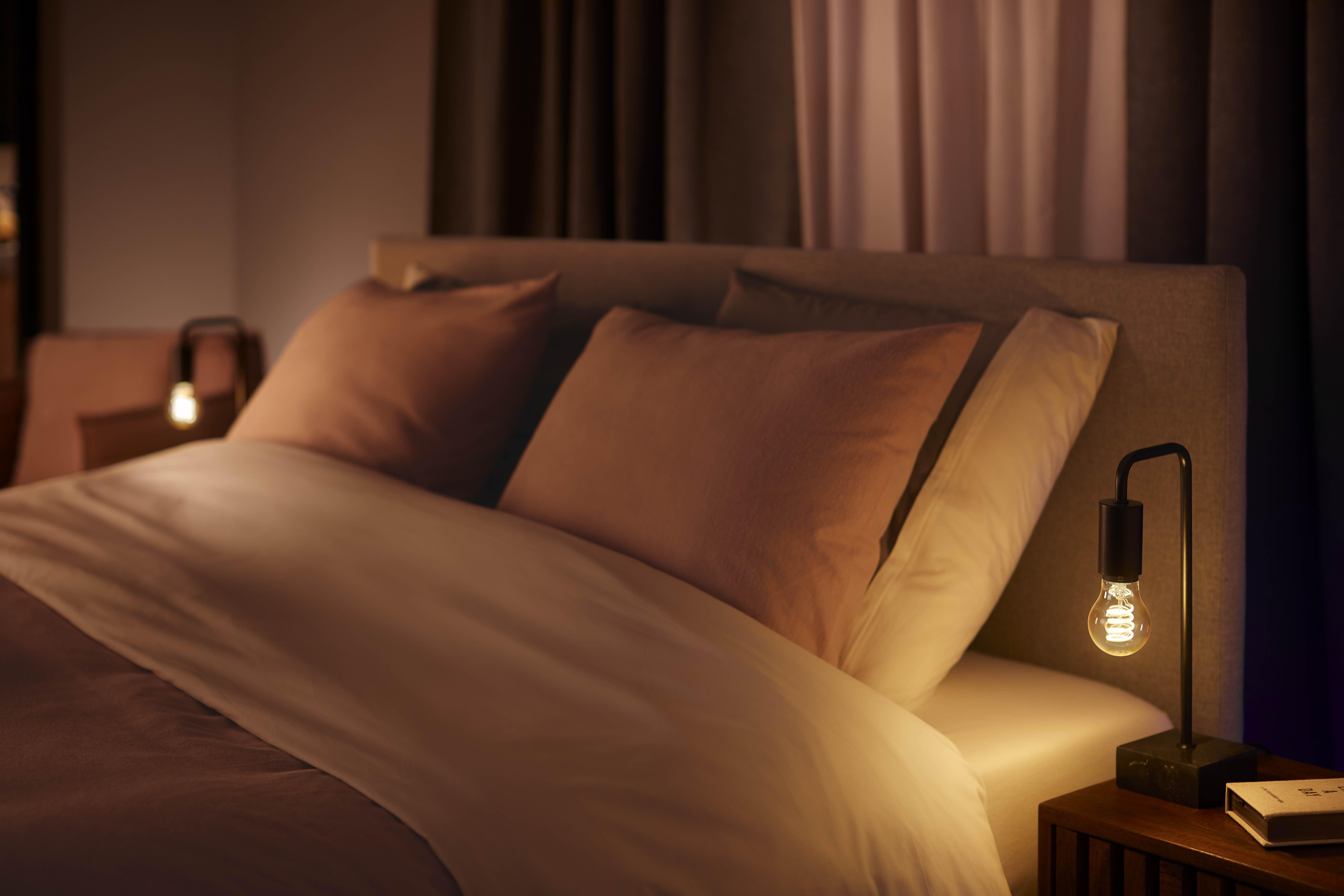 Schlafzimmerszene mit Bett, Kissen und Lampen. Weiche Beleuchtung schafft eine warme und einladende Atmosphäre.