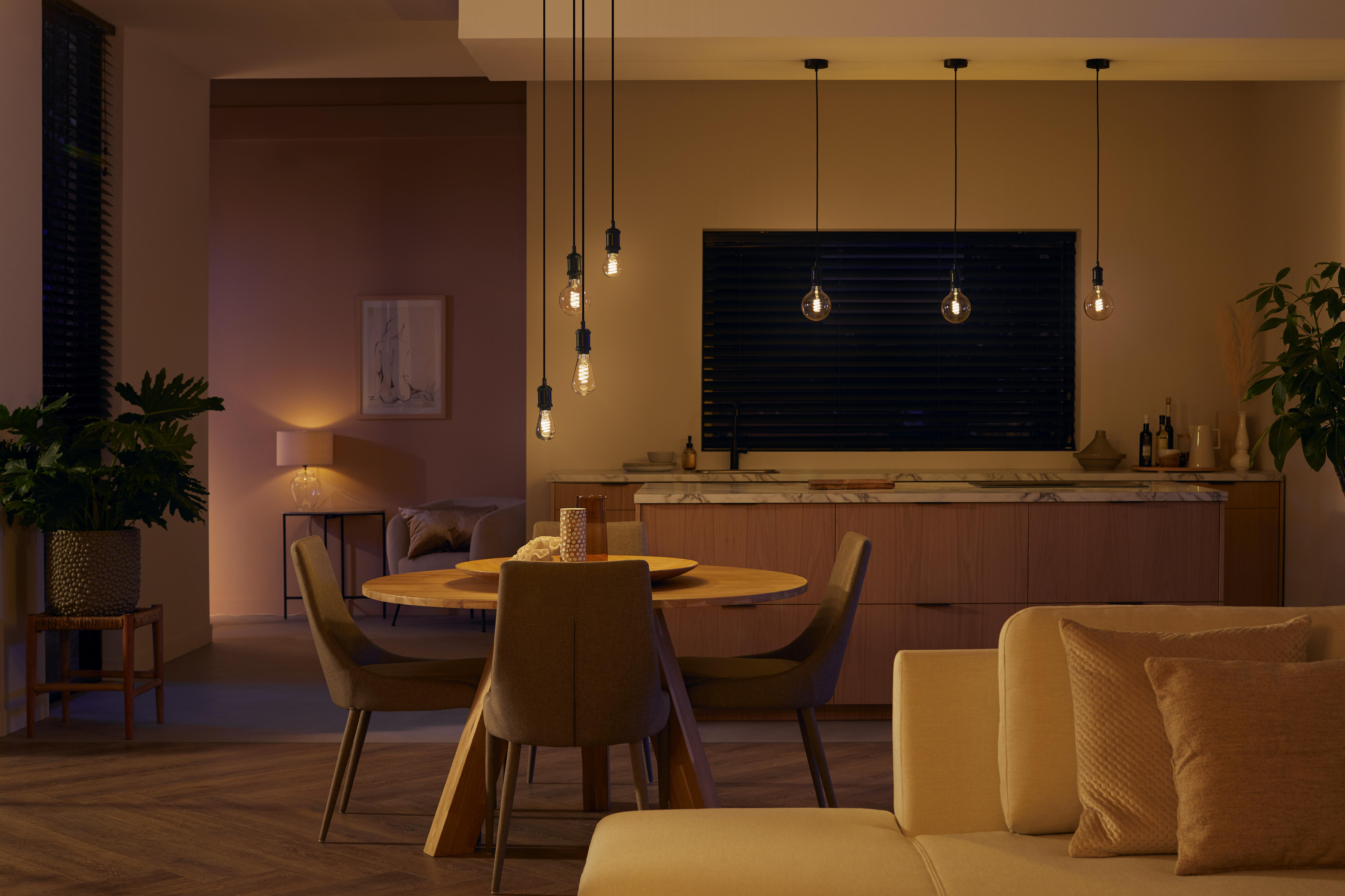 Wohnzimmer mit Hängelampen, Esstisch und Sofa. Warme, ambiente Beleuchtung.