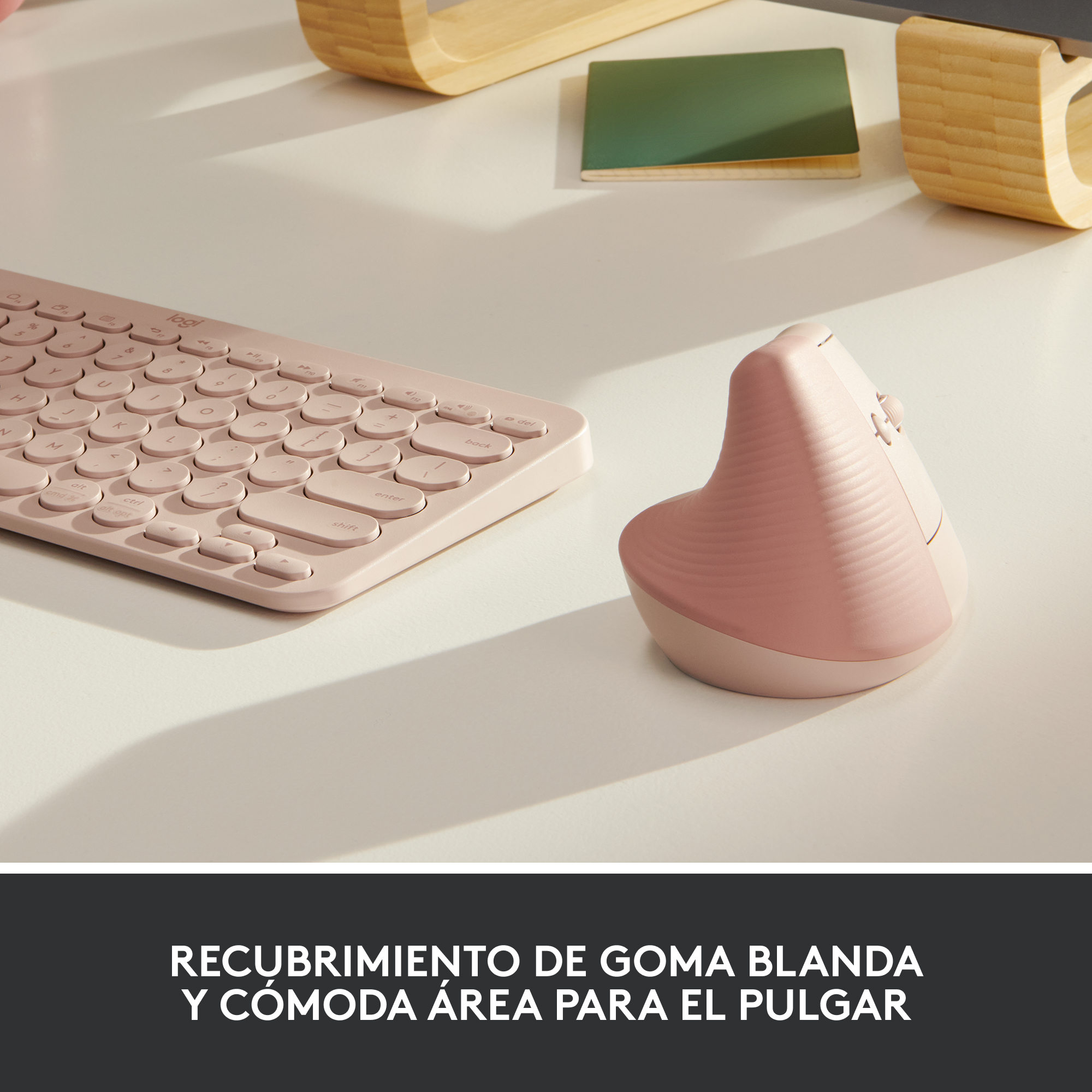 Un ratón y teclado ergonómicos rosas sobre un escritorio blanco. Fondo incluye madera y un objeto verde.