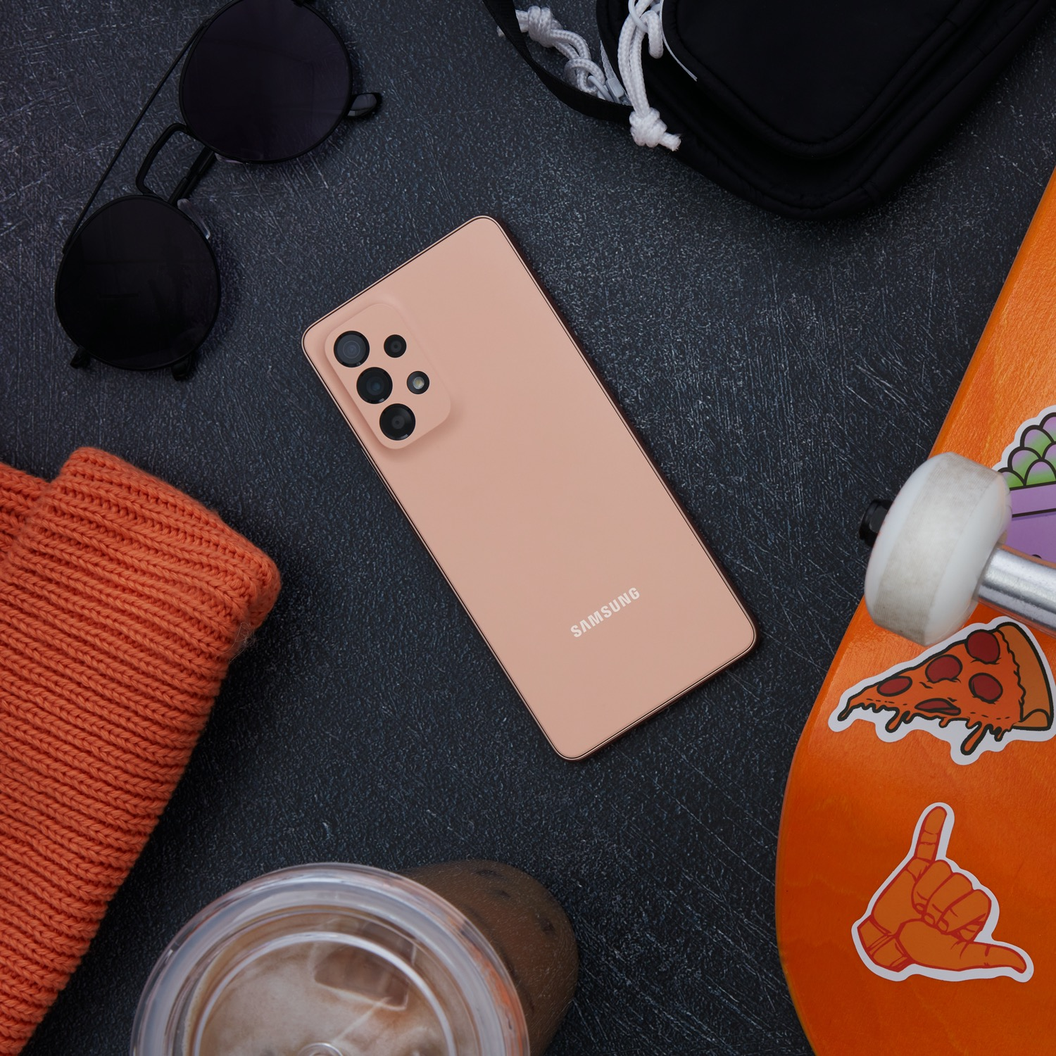 Vista superior de un teléfono melocotón junto a accesorios como gafas de sol y monopatín.
