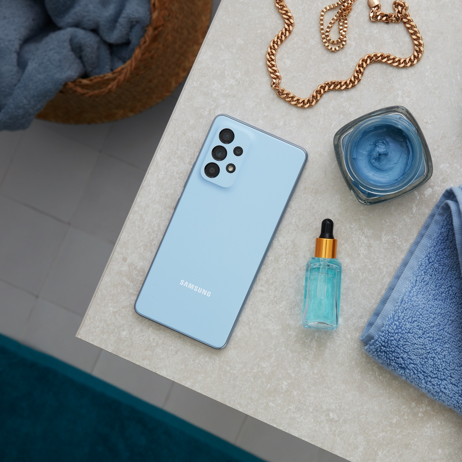 Un teléfono Samsung azul claro sobre una encimera con productos de belleza.