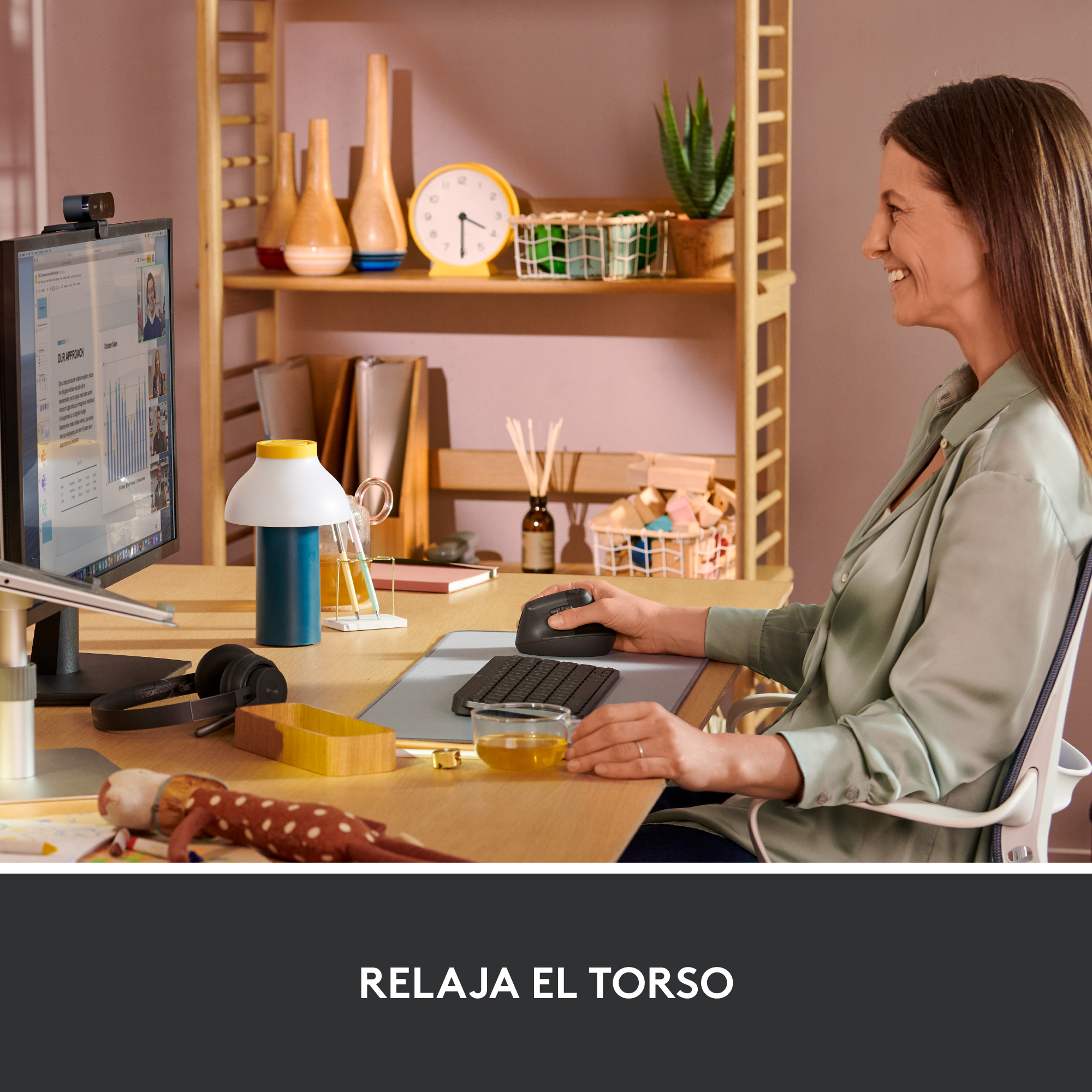 Mujer trabajando en un escritorio con computadora y ratón. Hay una lámpara, auriculares y otros objetos.