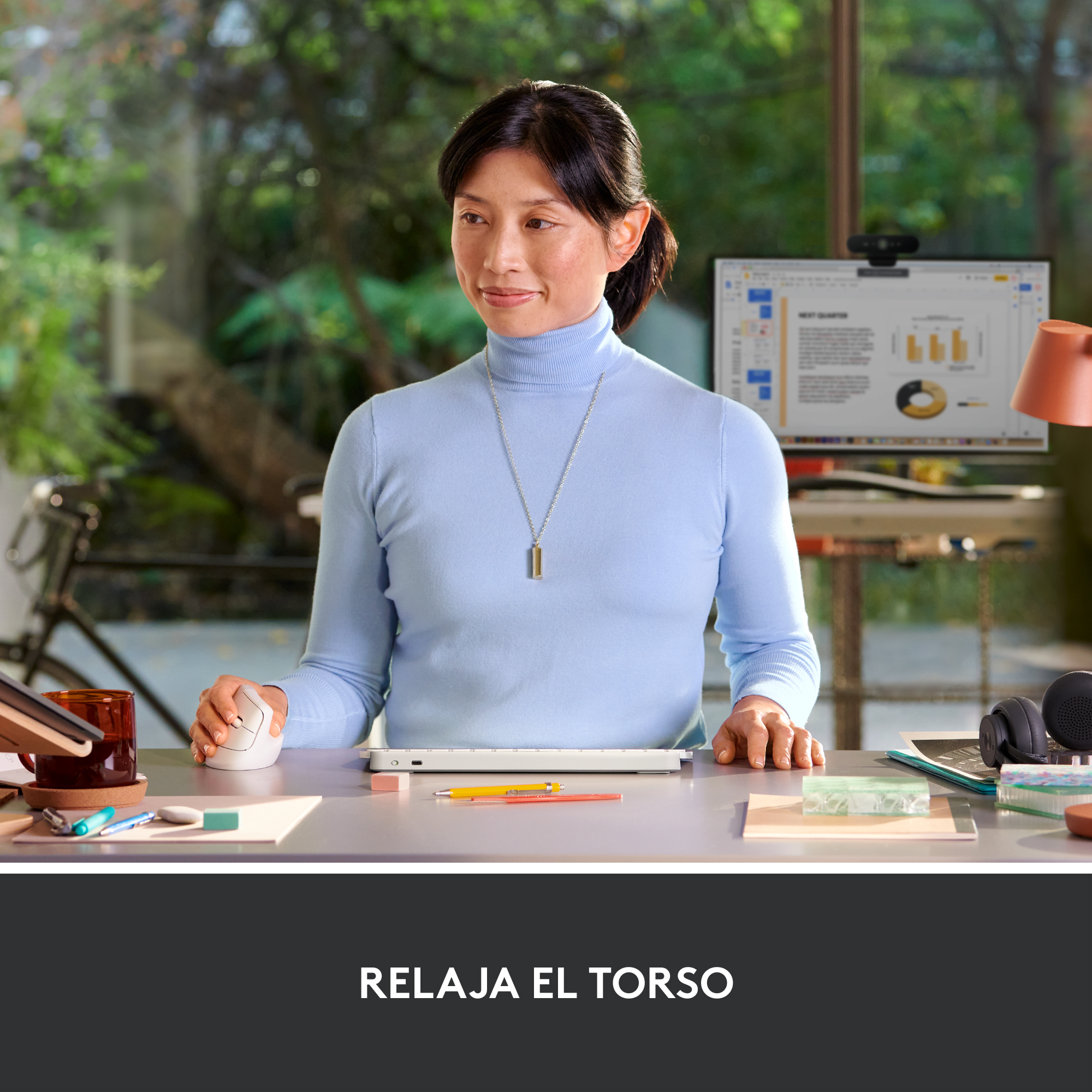 Mujer en el escritorio con monitor y accesorios. Está sentada y trabajando en un escritorio.