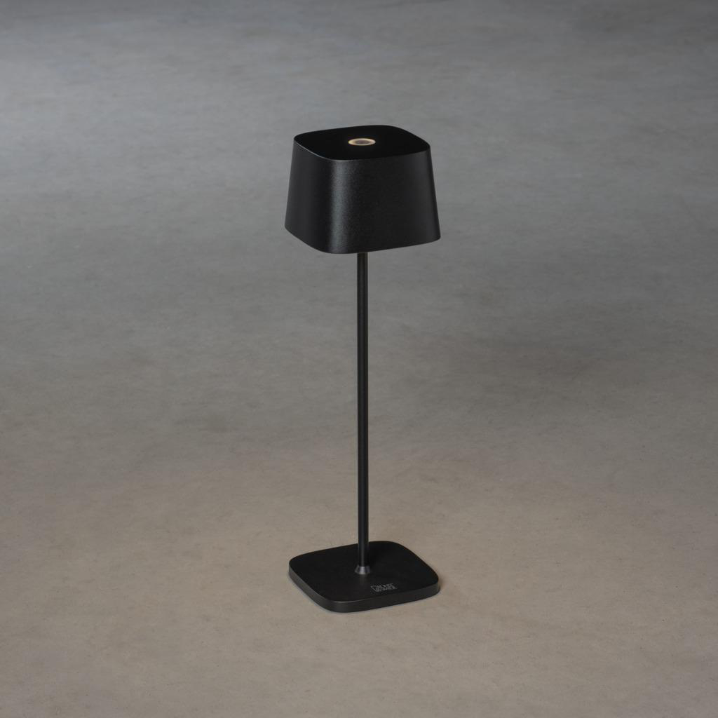 Schwarze Lampe mit quadratischem Sockel und Schirm. Dunkelgrauer Hintergrund.