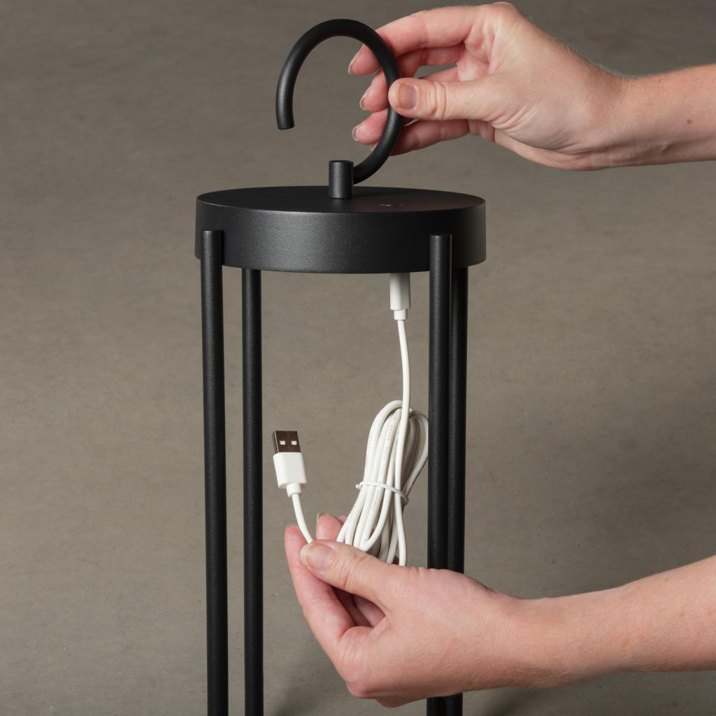 Hände, die eine schwarze Lampe zusammenbauen. Die Lampe hat eine kreisförmige Oberseite und drei vertikale Stützen. Ein weißes USB-Kabel.