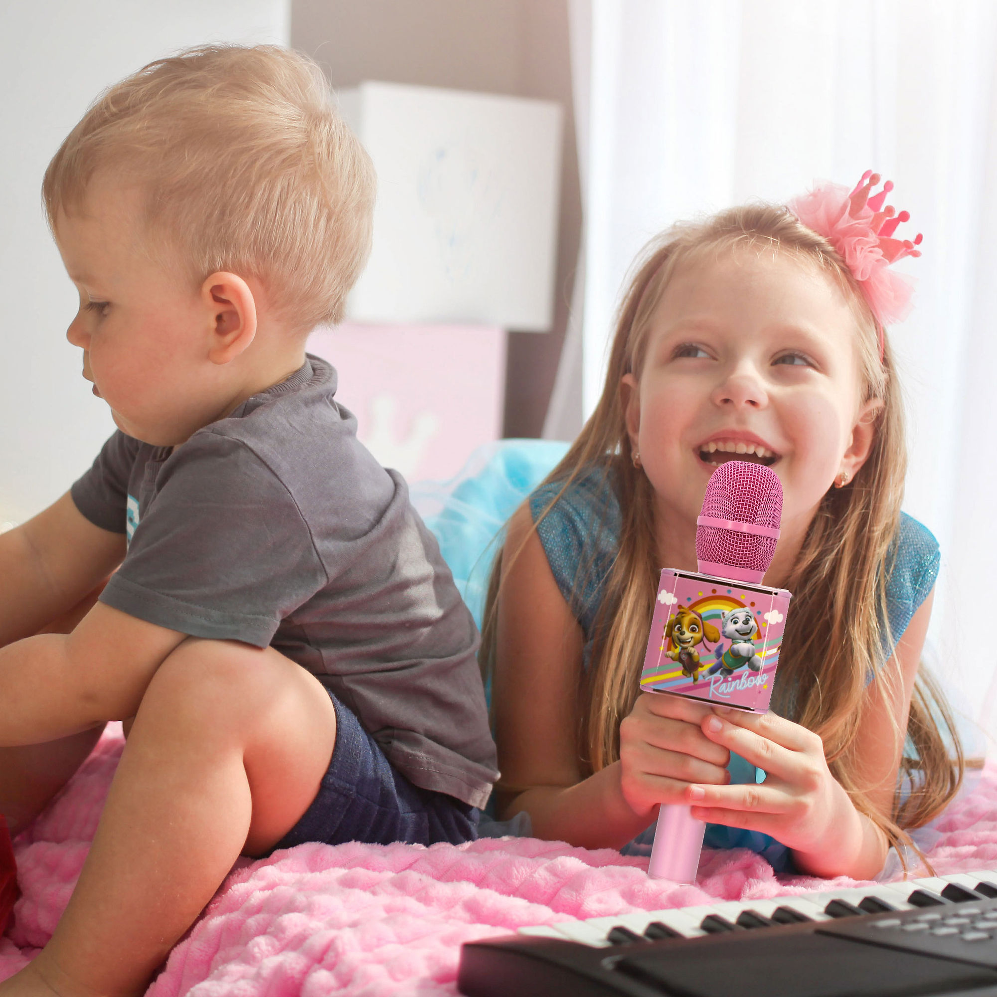 Deux enfants chantant dans un microphone rose. Un enfant est assis.