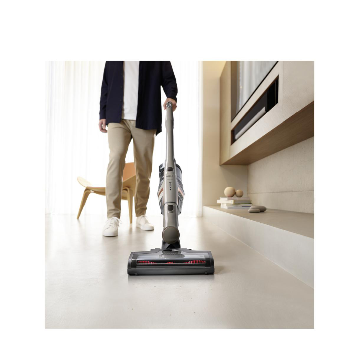 Person saugt einen Raum mit einem kabellosen Staubsauger, modernes Interieur.