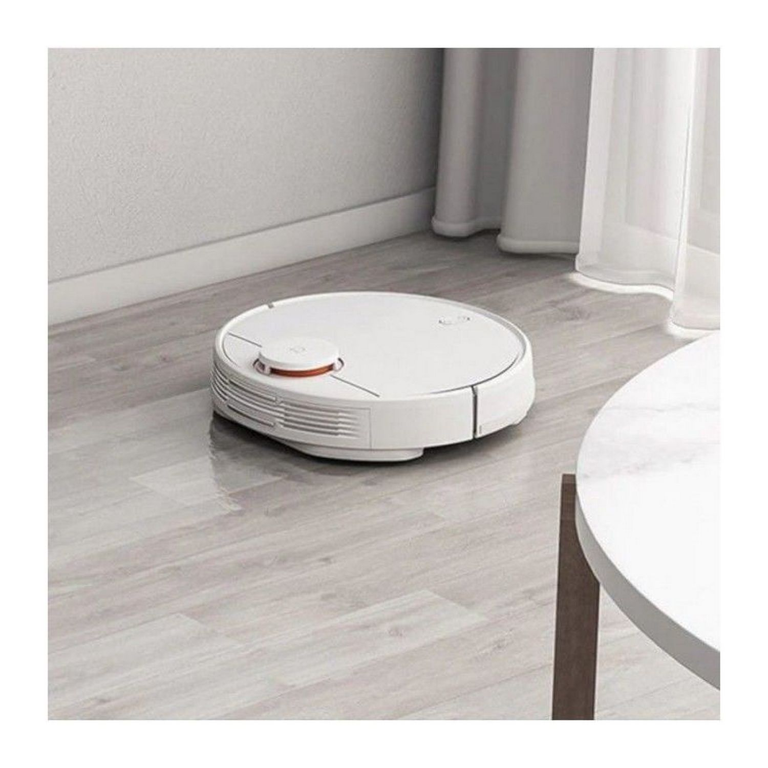 Aspiradora robot blanca sobre suelo de madera, cerca de mesa y pared blancas.