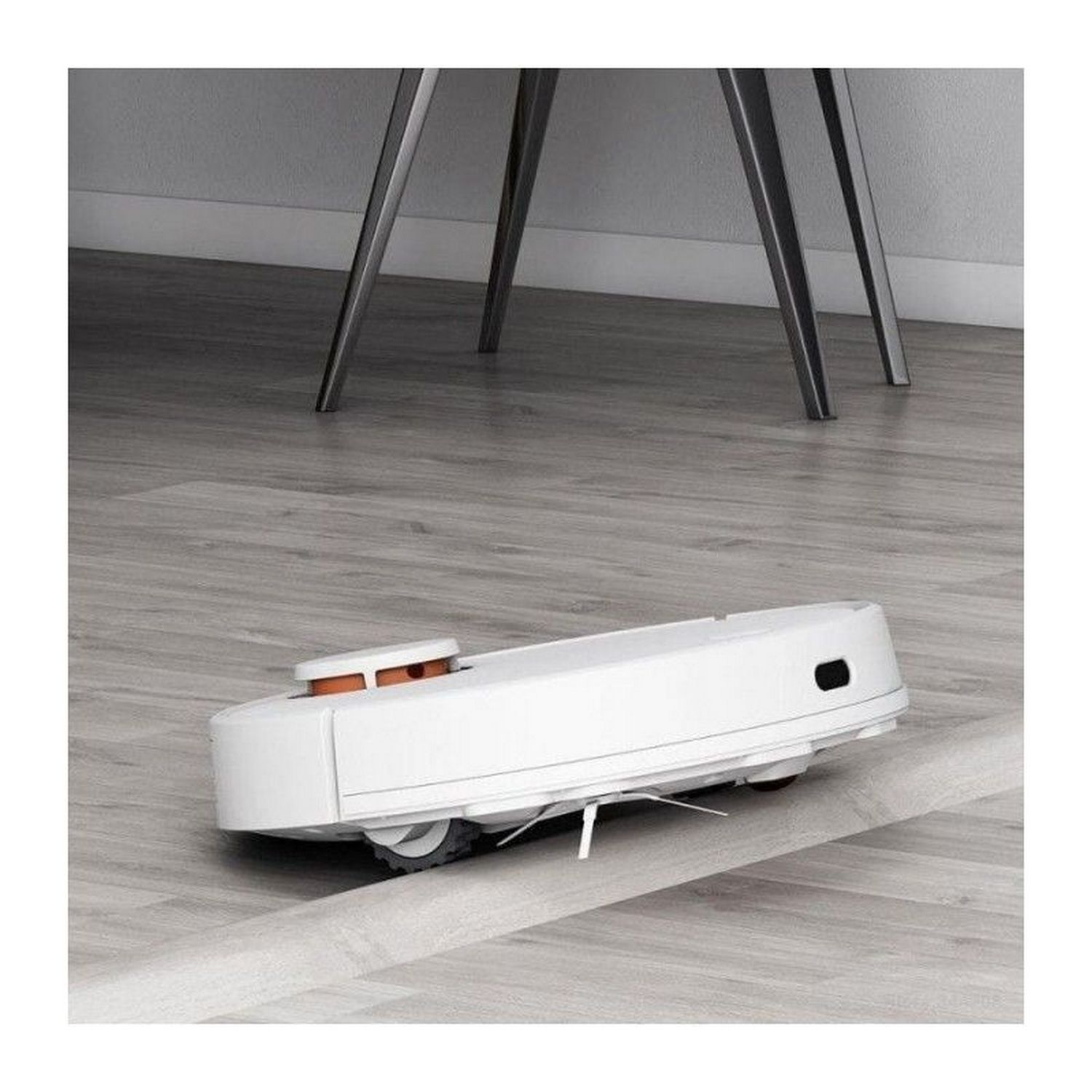 Aspiradora robot blanca en un piso de madera, con un marco negro.