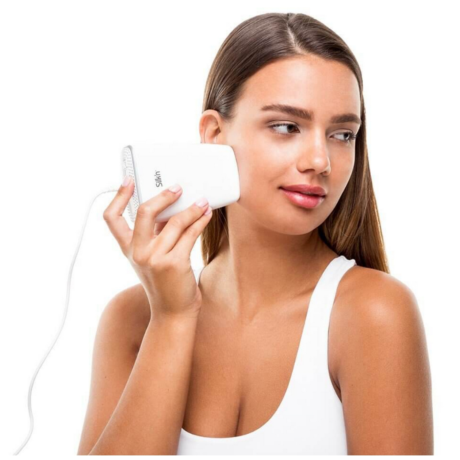 Mujer usando dispositivo blanco para el cuidado de la piel en su rostro, top blanco.