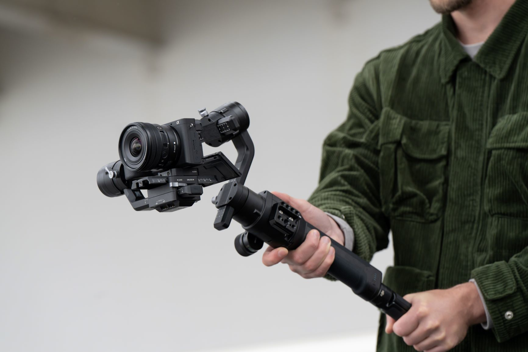 Ein Mann hält eine Kamera mit einem Gimbal. Kamera und Gimbal sind schwarz. Der Mann trägt eine grüne Jacke.