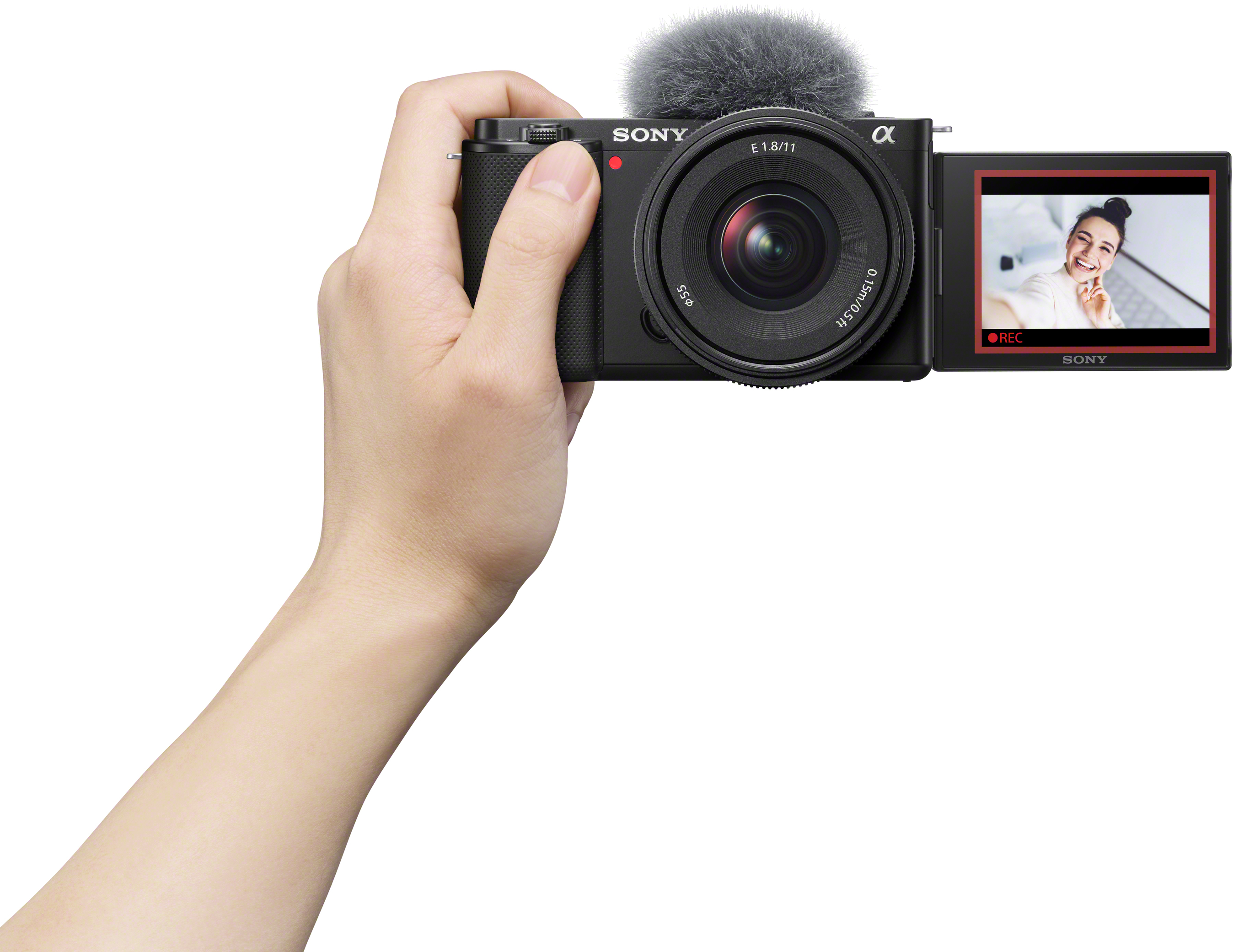 Eine schwarze Sony-Kamera mit Mikrofon wird von einer Hand gehalten. Der Bildschirm zeigt eine lächelnde Frau.