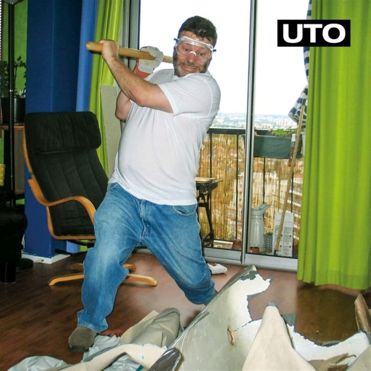 Mann, der mit einem Vorschlaghammer eine Wand durchbricht, Schutzbrille trägt, in einem Raum.