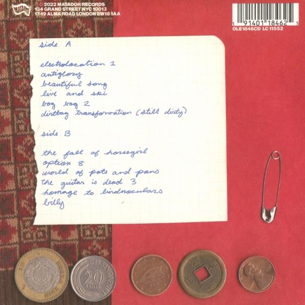 Rückseite eines Schallplattenalbums mit handgeschriebenen Songtiteln. Münzen und eine Sicherheitsnadel liegen ebenfalls auf dem roten Hintergrund.