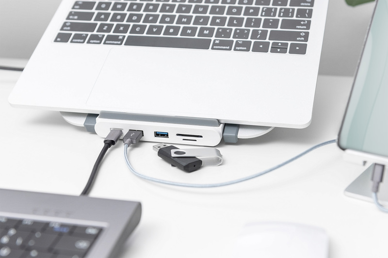 Laptop auf einem weißen Schreibtisch mit angeschlossenem Hub, USB-Laufwerken und Kabeln.