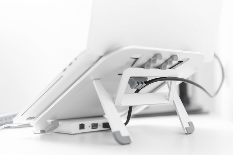 Ein weißer Laptop auf einem weißen Ständer, mit Kabeln und einem Port-Hub, auf einer weißen Oberfläche.