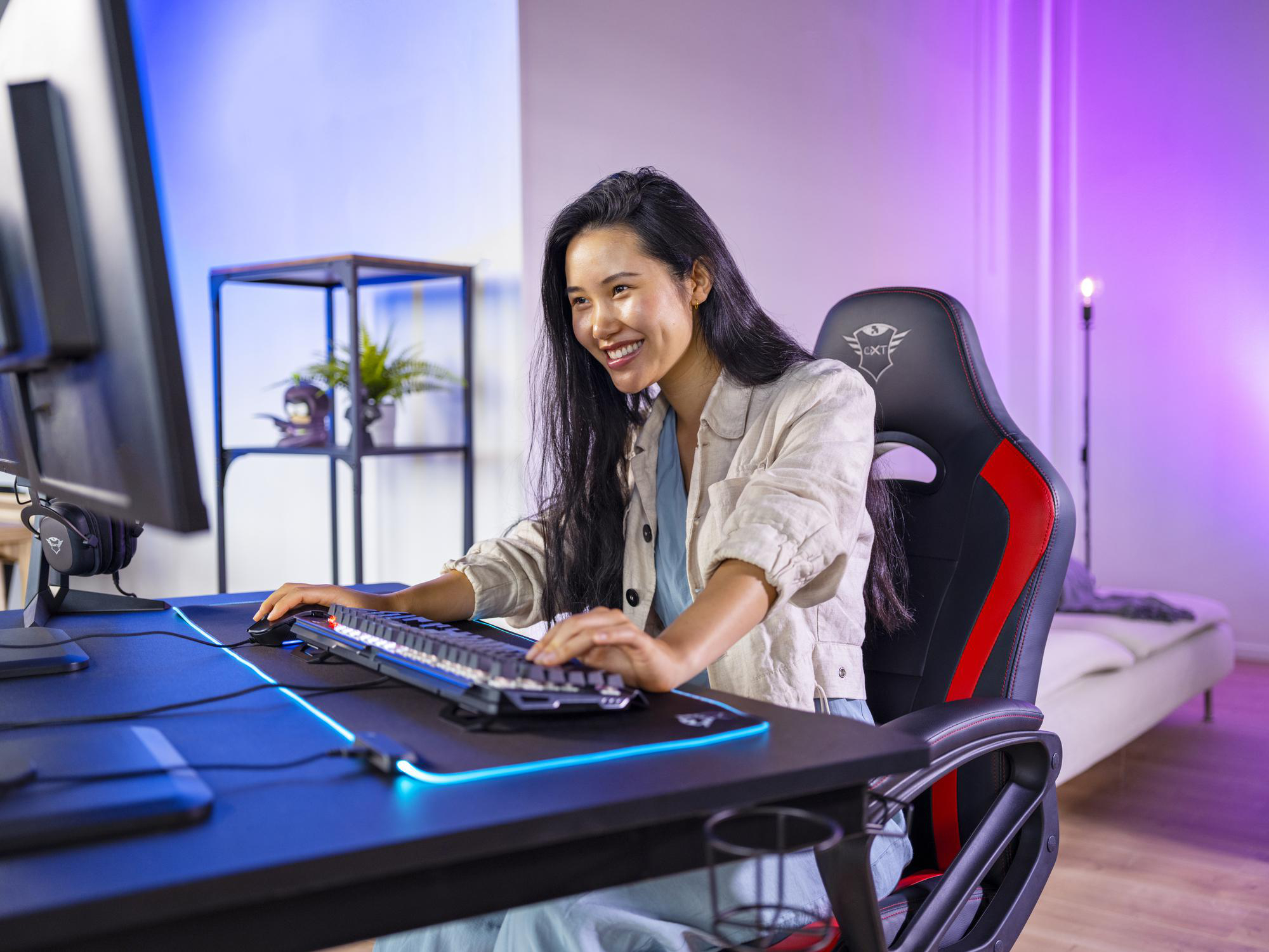 Eine Frau lächelt, während sie ein Computerspiel an einem Schreibtisch mit Tastatur und Monitor spielt.