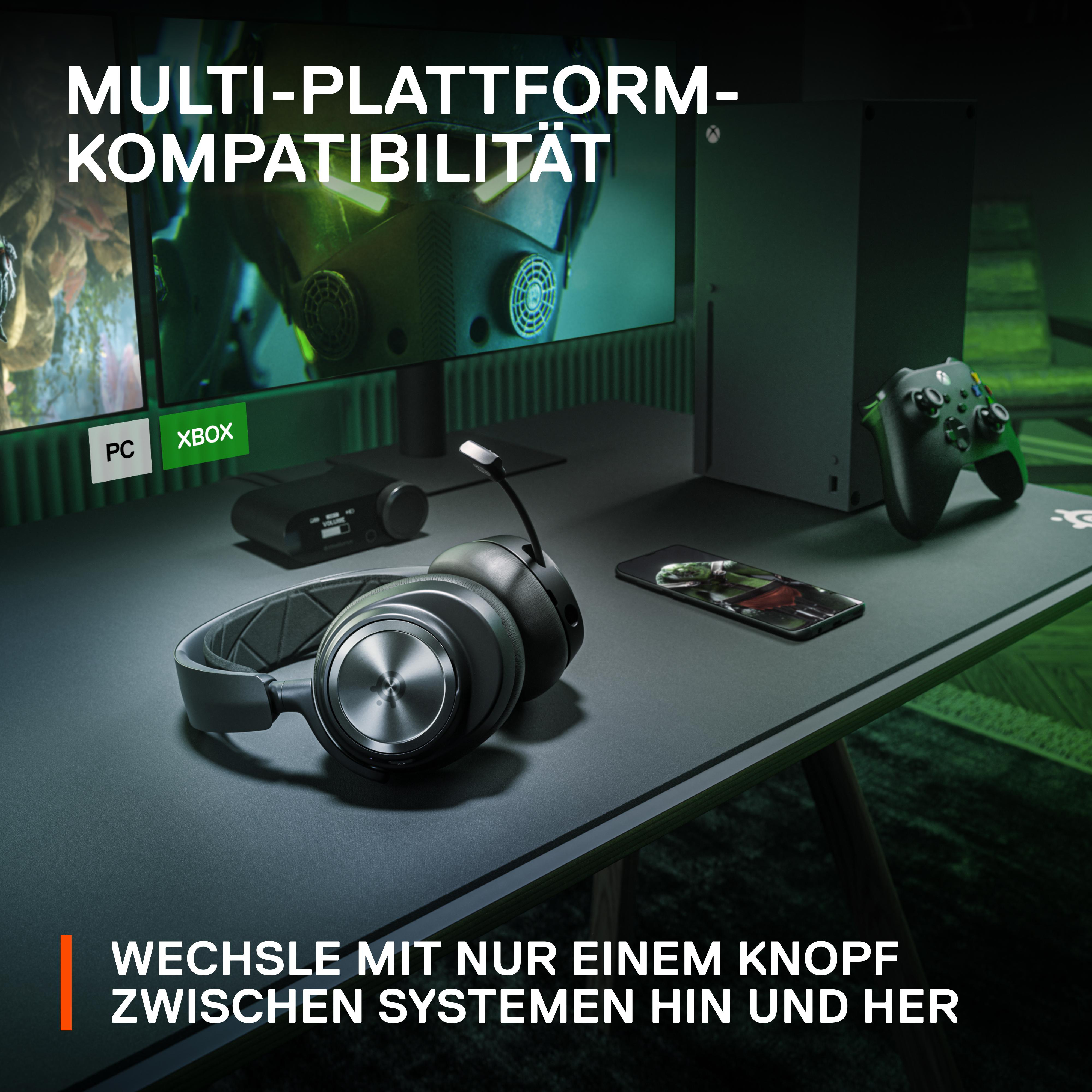 Kopfhörer und Telefon auf einem Schreibtisch, PC und Xbox-Monitor im Hintergrund.