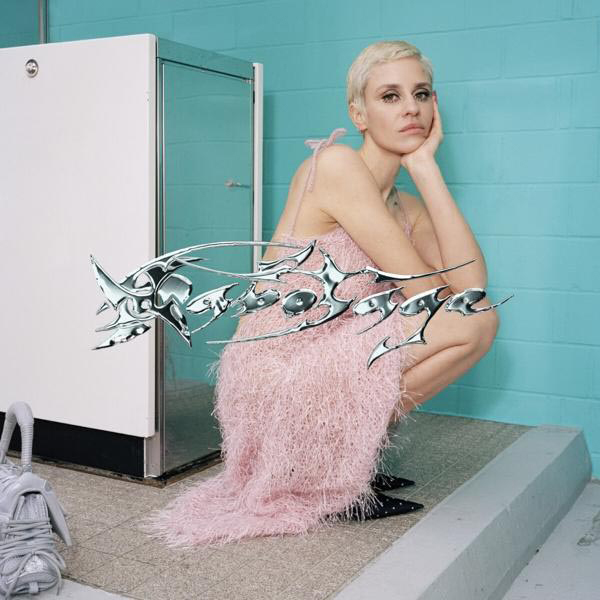 Eine Frau mit kurzen blonden Haaren in einem rosa Kleid hockt neben einer weißen und blauen Wand.