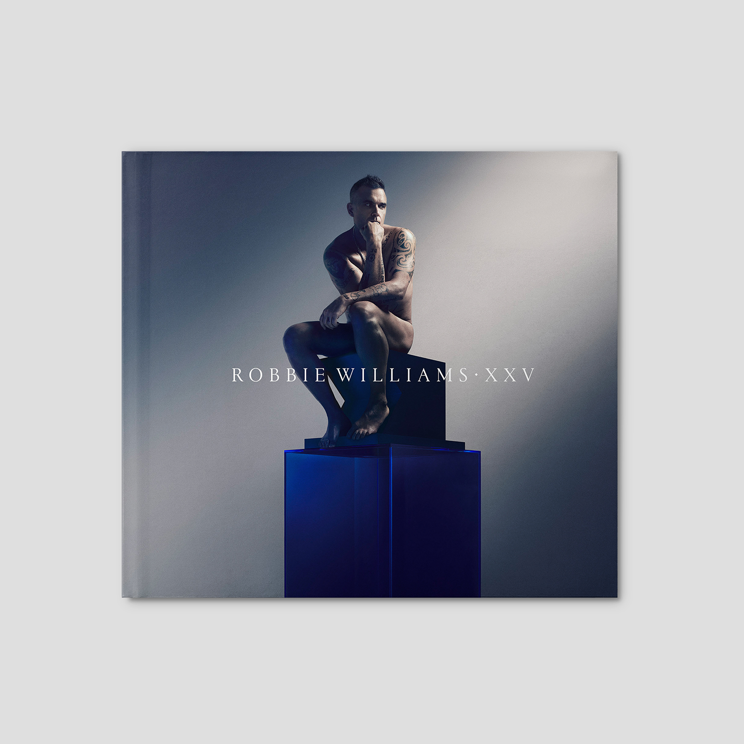 Albumcover mit nacktem Mann auf blauem Podest, sitzend, grauer Hintergrund, Text.