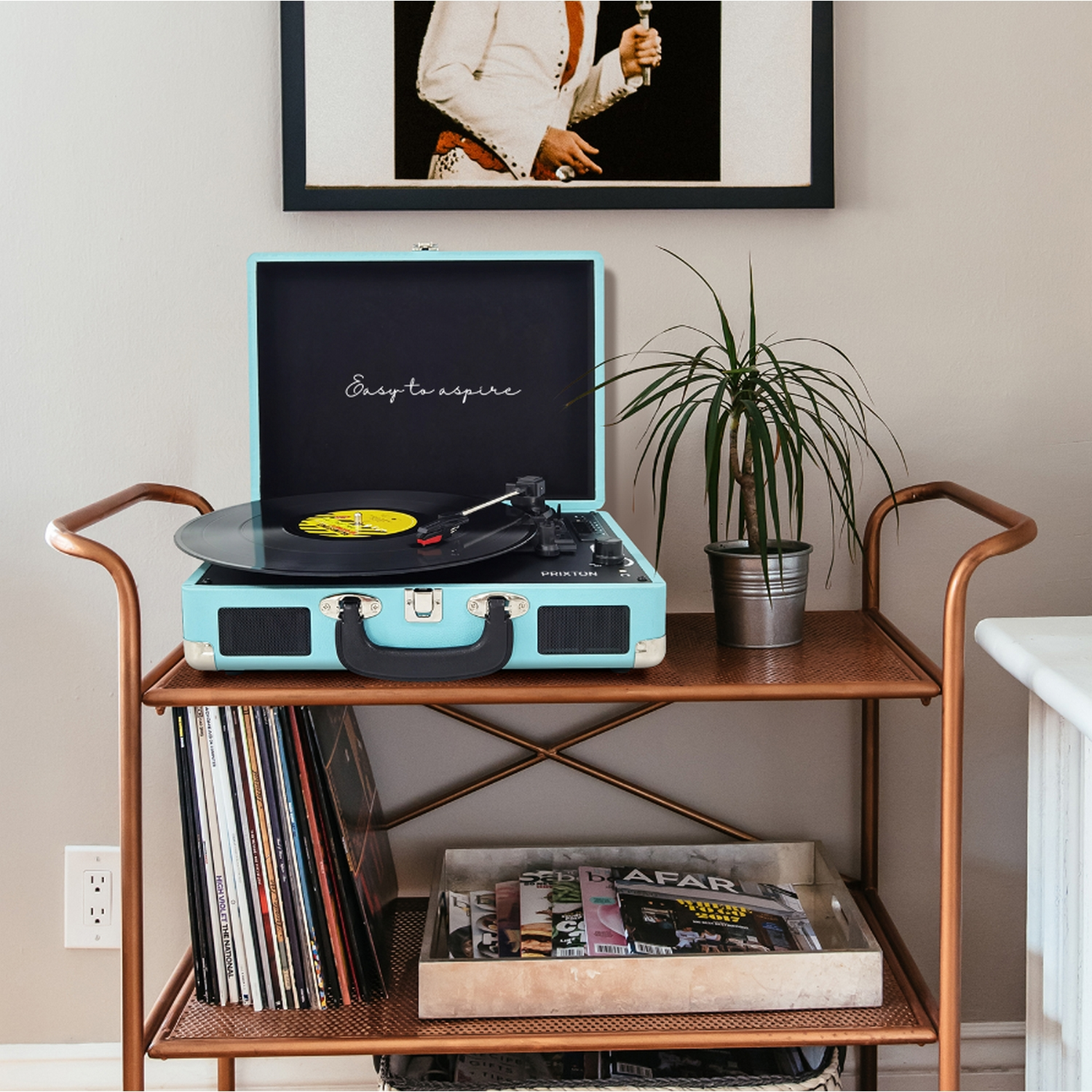 Tocadiscos turquesa en carrito de cobre con vinilos, planta y foto de Elvis.