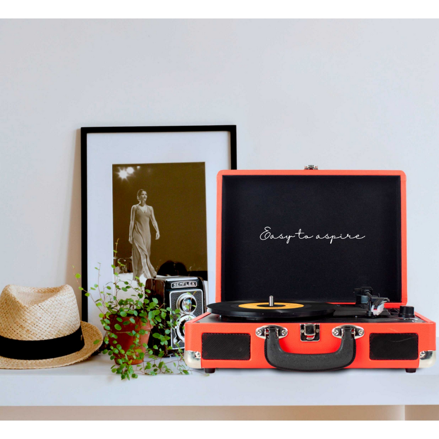 Un tocadiscos en un estante blanco con una foto enmarcada, un sombrero y una cámara.