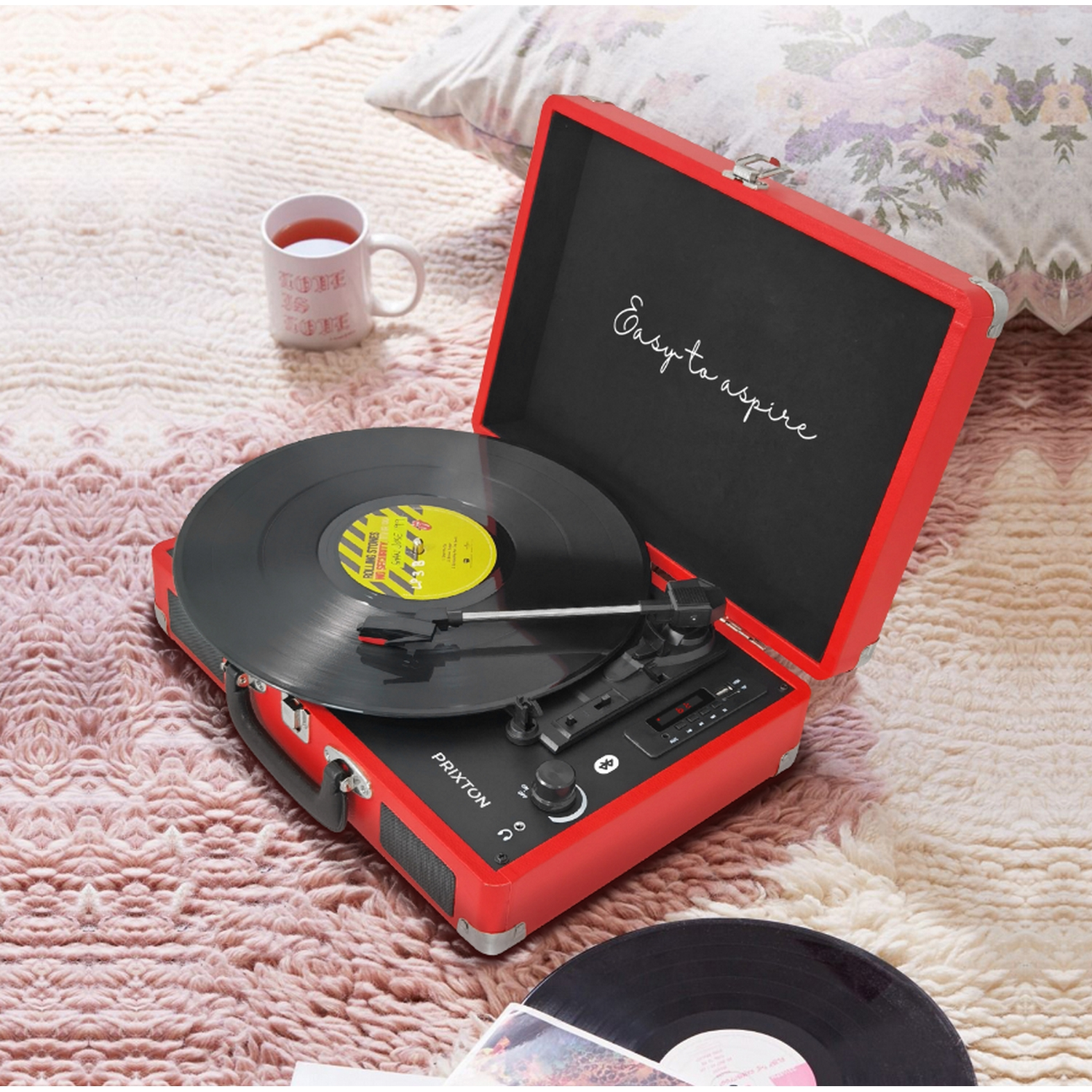 Tocadiscos rojo con disco. Una taza y una almohada en el fondo.