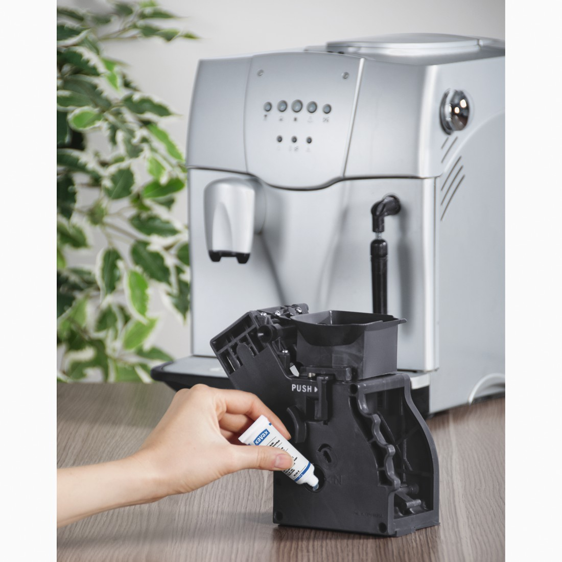 A hand applies lubricant to a black coffee machine component.