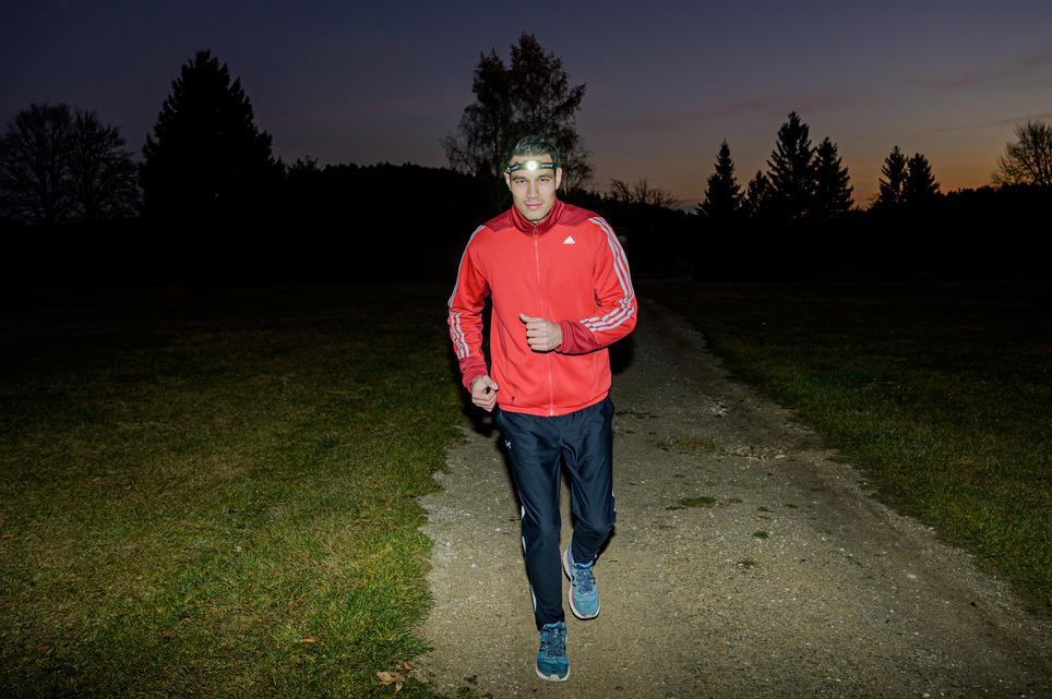 Ein Mann joggt im Dunkeln auf einem Pfad, mit Stirnlampe und roter Jacke.