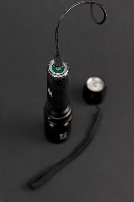 Schwarze Taschenlampe mit Handschlaufe und Ladekabel. Die Oberseite ist geöffnet.