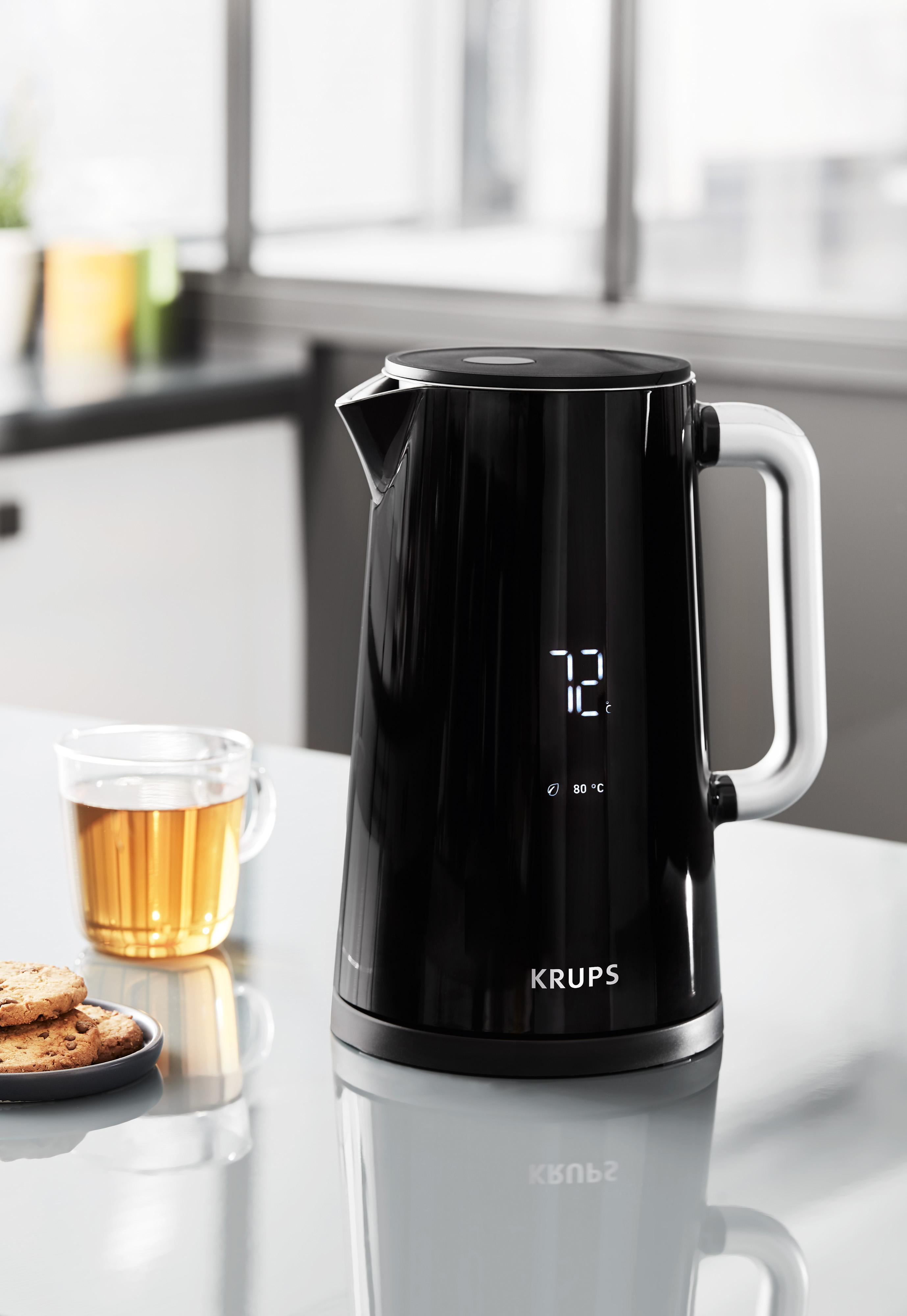 Schwarzer Wasserkocher mit weißem Griff, neben einer Teetasse und Keksen.
