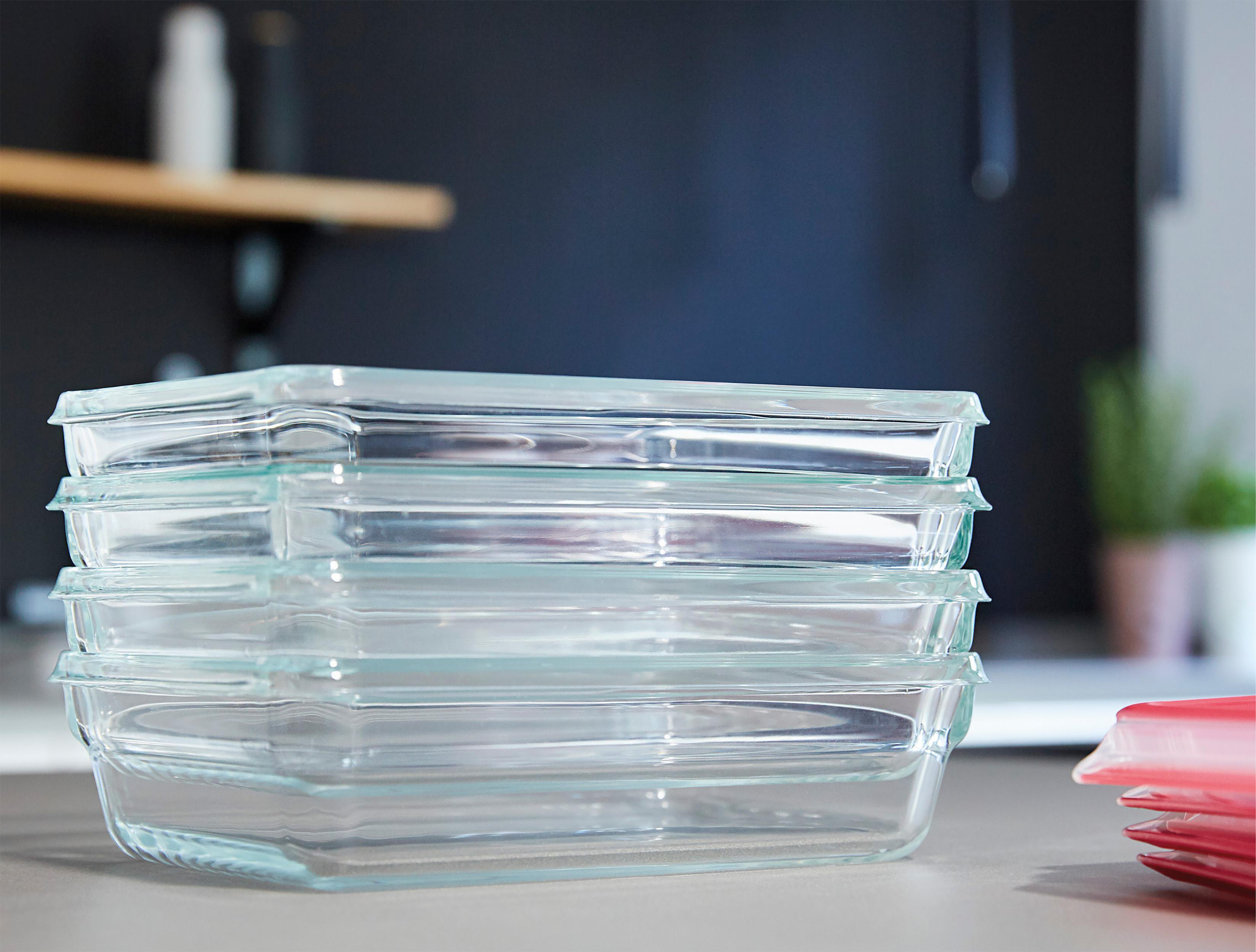 Ein Stapel klarer Glas-Backformen, mit einem teilweise sichtbaren roten Deckel im Hintergrund.