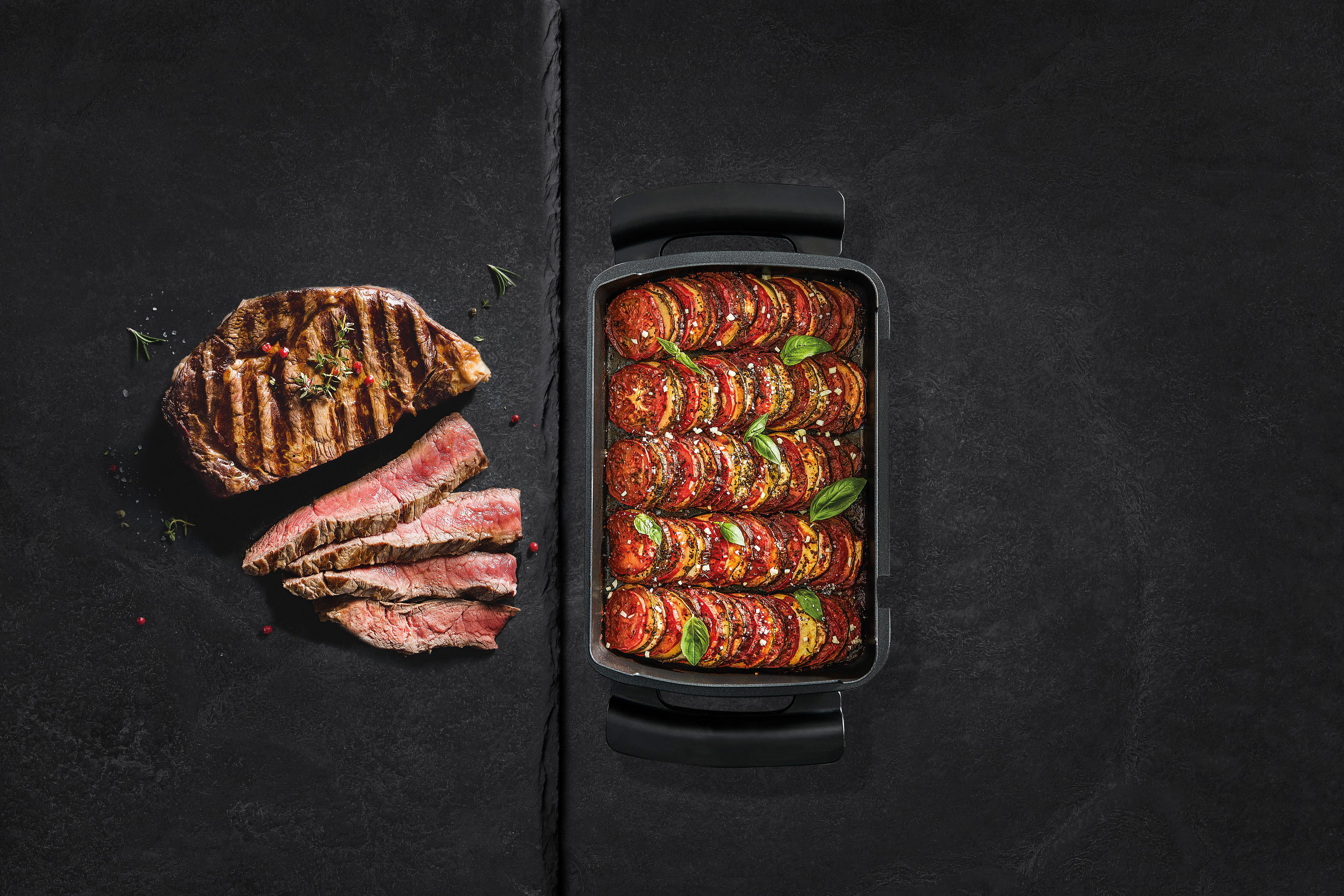 Gegrilltes Steak und geschnittenes Steak mit Ratatouille, schwarzer Hintergrund.