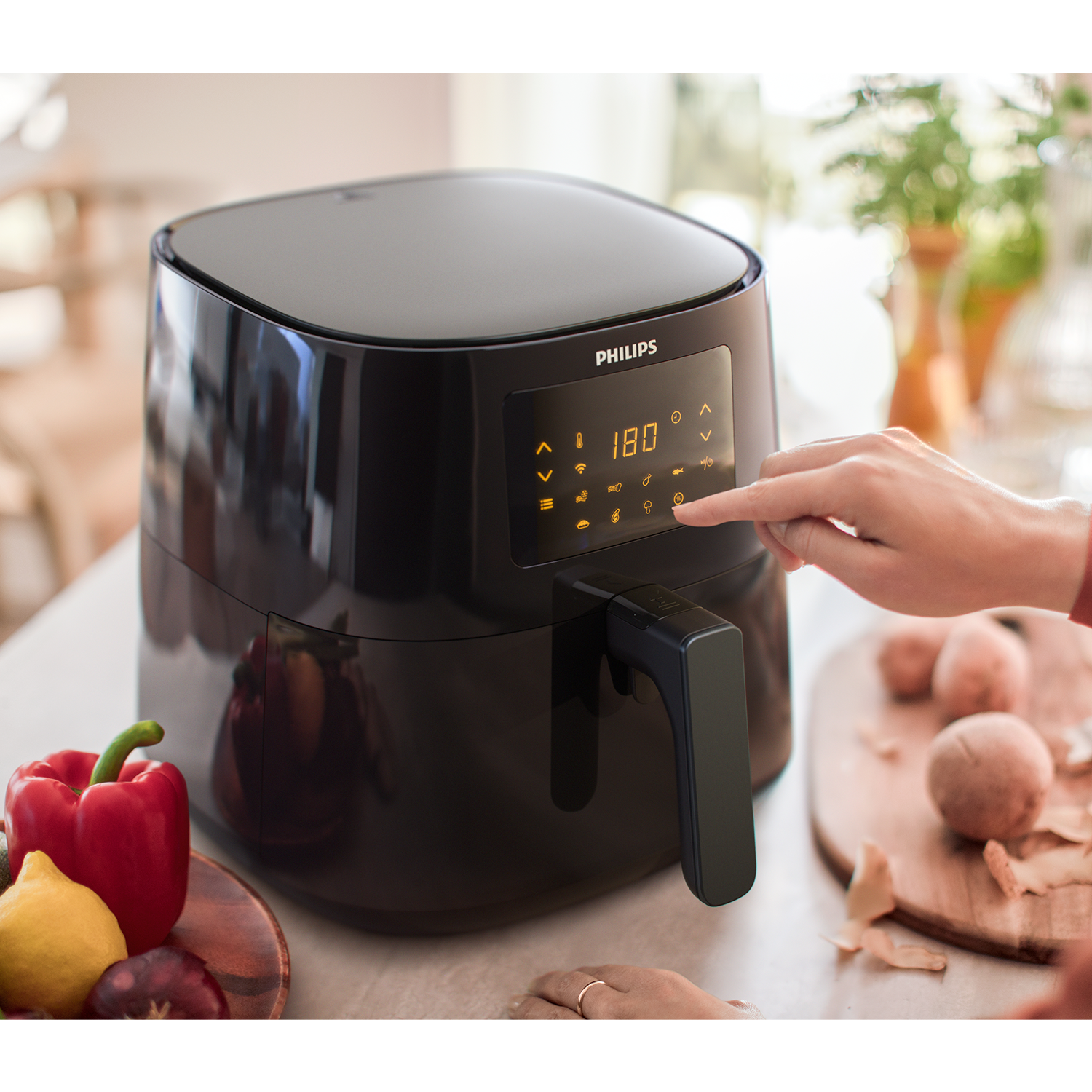 Una mano usando los controles de una freidora de aire Philips negra, con alimentos cerca.
