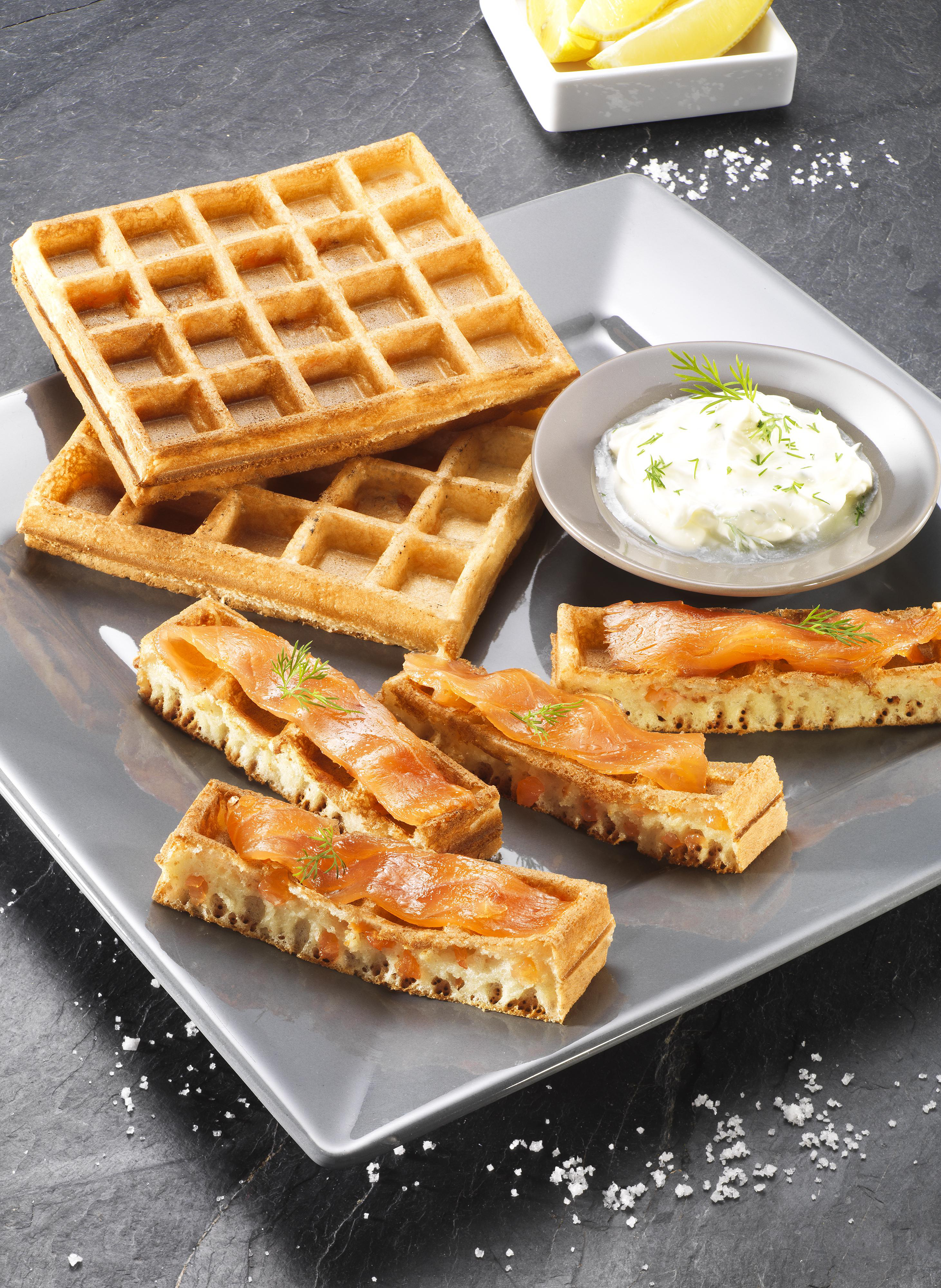 Waffeln mit Räucherlachs und Sauerrahm auf grauem Teller, mit Zitronenscheiben.
