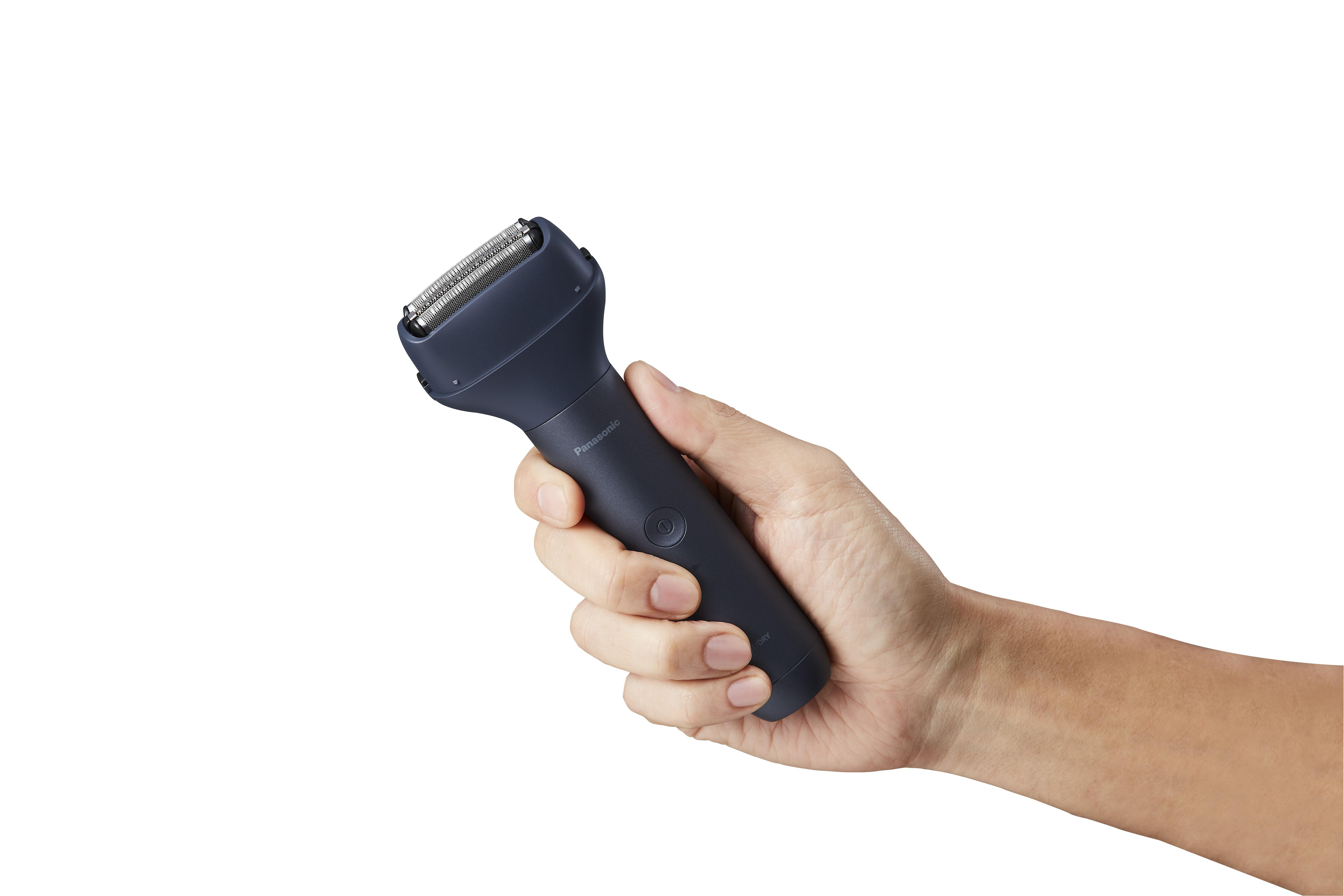 Hand einer Person, die einen dunkelblauen Elektrorasierer vor weißem Hintergrund hält.